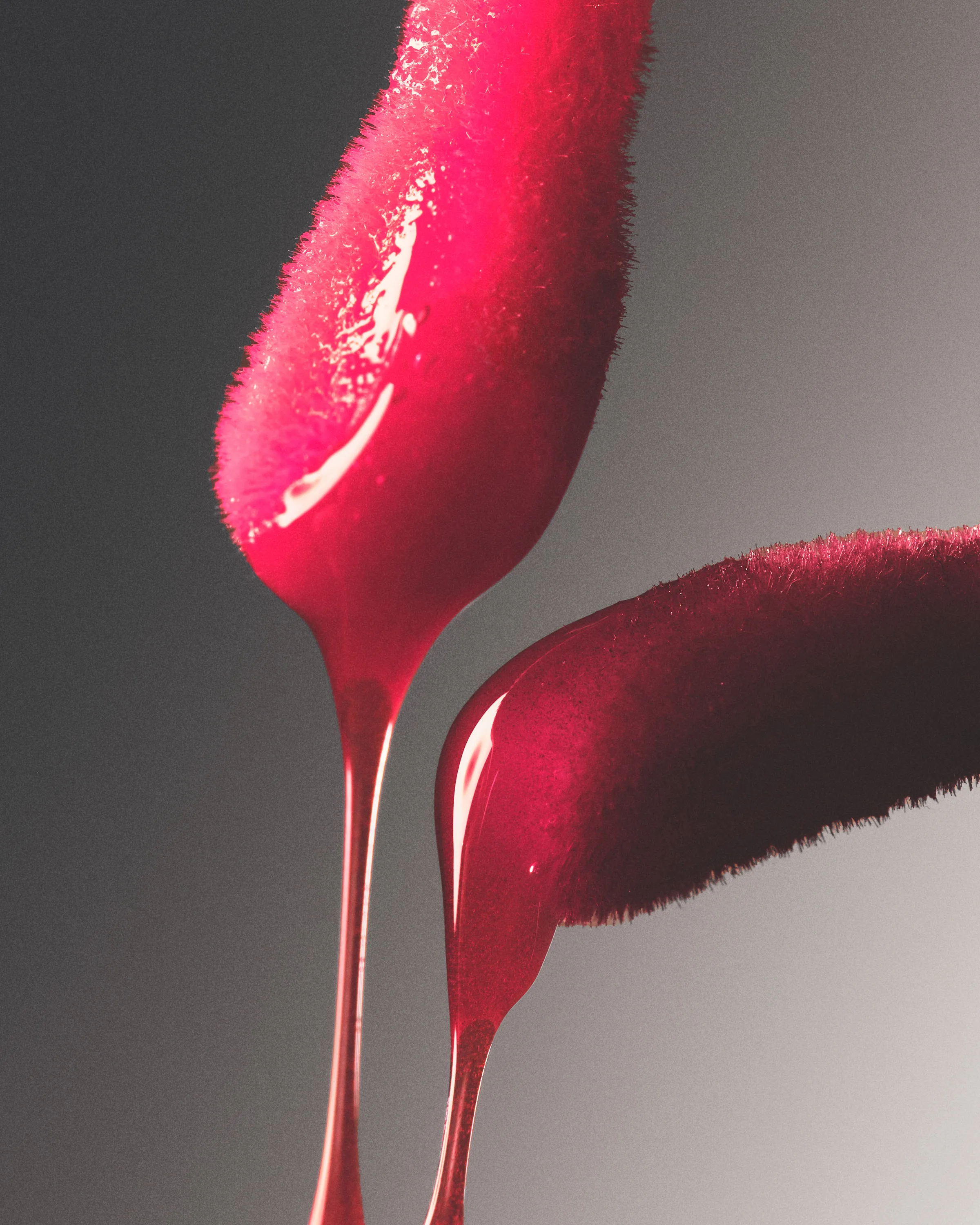 Two red flocked lip gloss applicators dripping glossy pink liquid against a grey gradient, for Kylie Cosmetics.