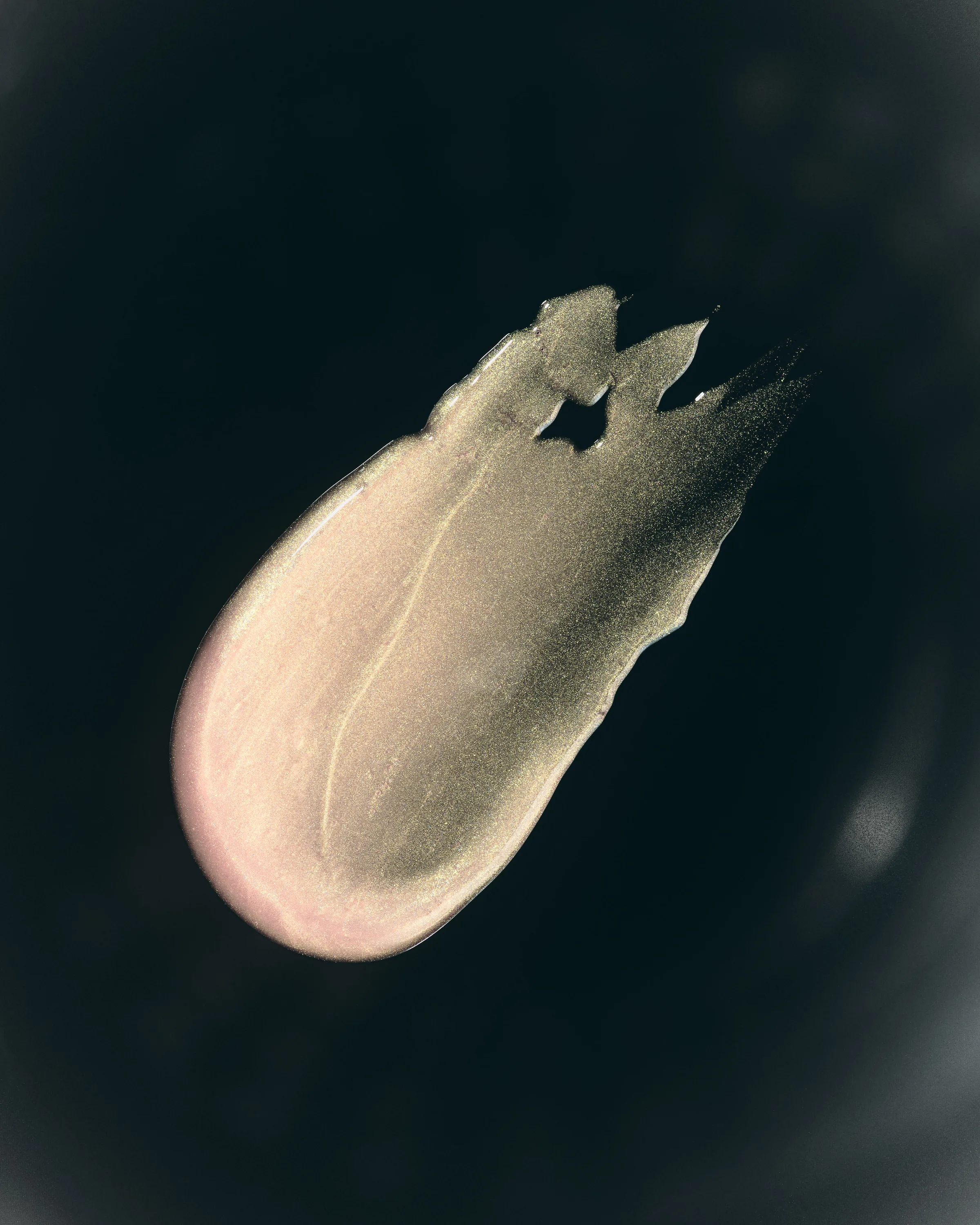 Swatch of pale gold shimmering lip glaze smeared across a black background, for Kylie Cosmetics.