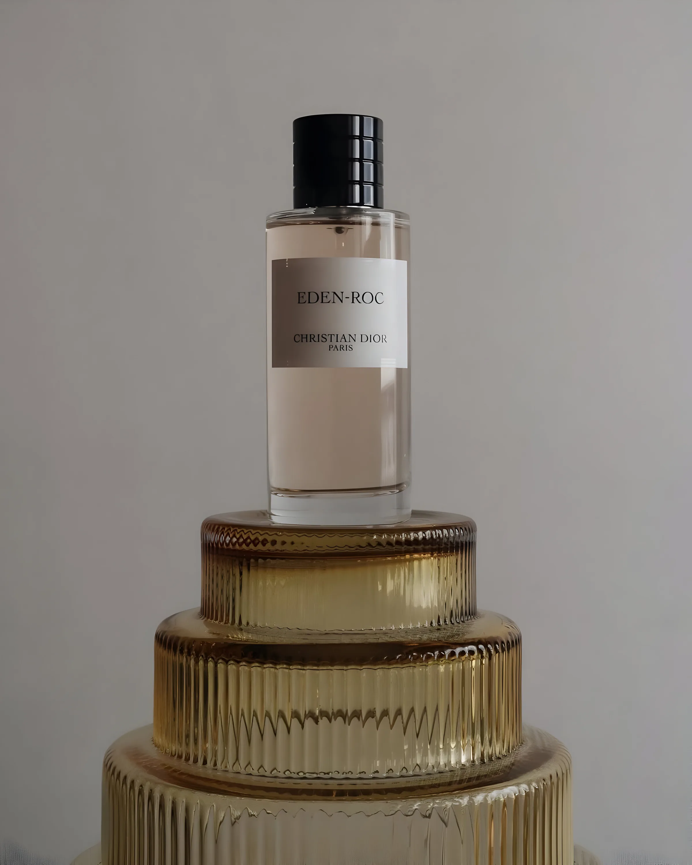 Eden-Roc perfume bottle on stacked amber ribbed glass tiers against a grey wall, for Dior.