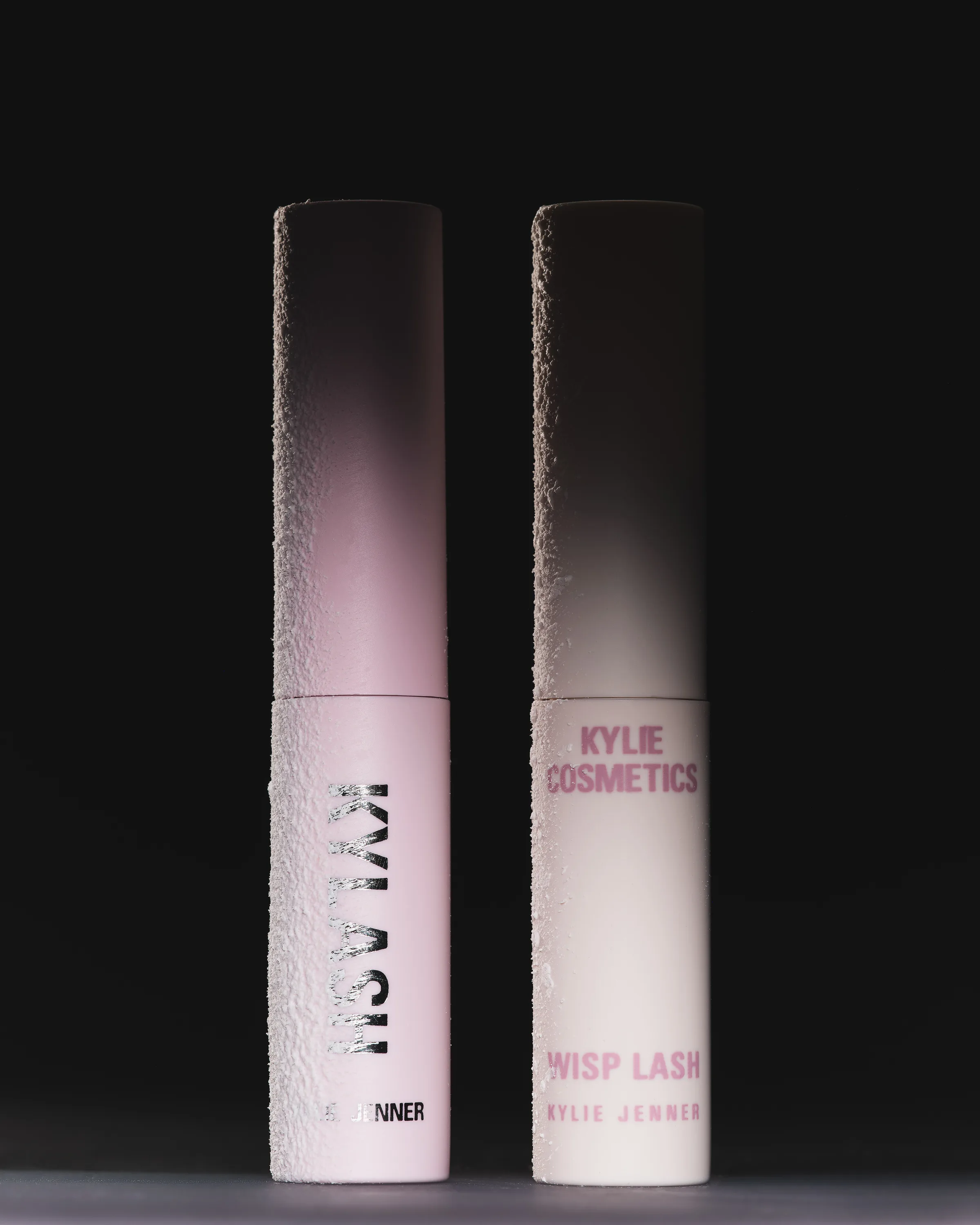 Kylash and Wisp Lash mini mascaras with frosted texture standing against a dark background, for Kylie Cosmetics.
