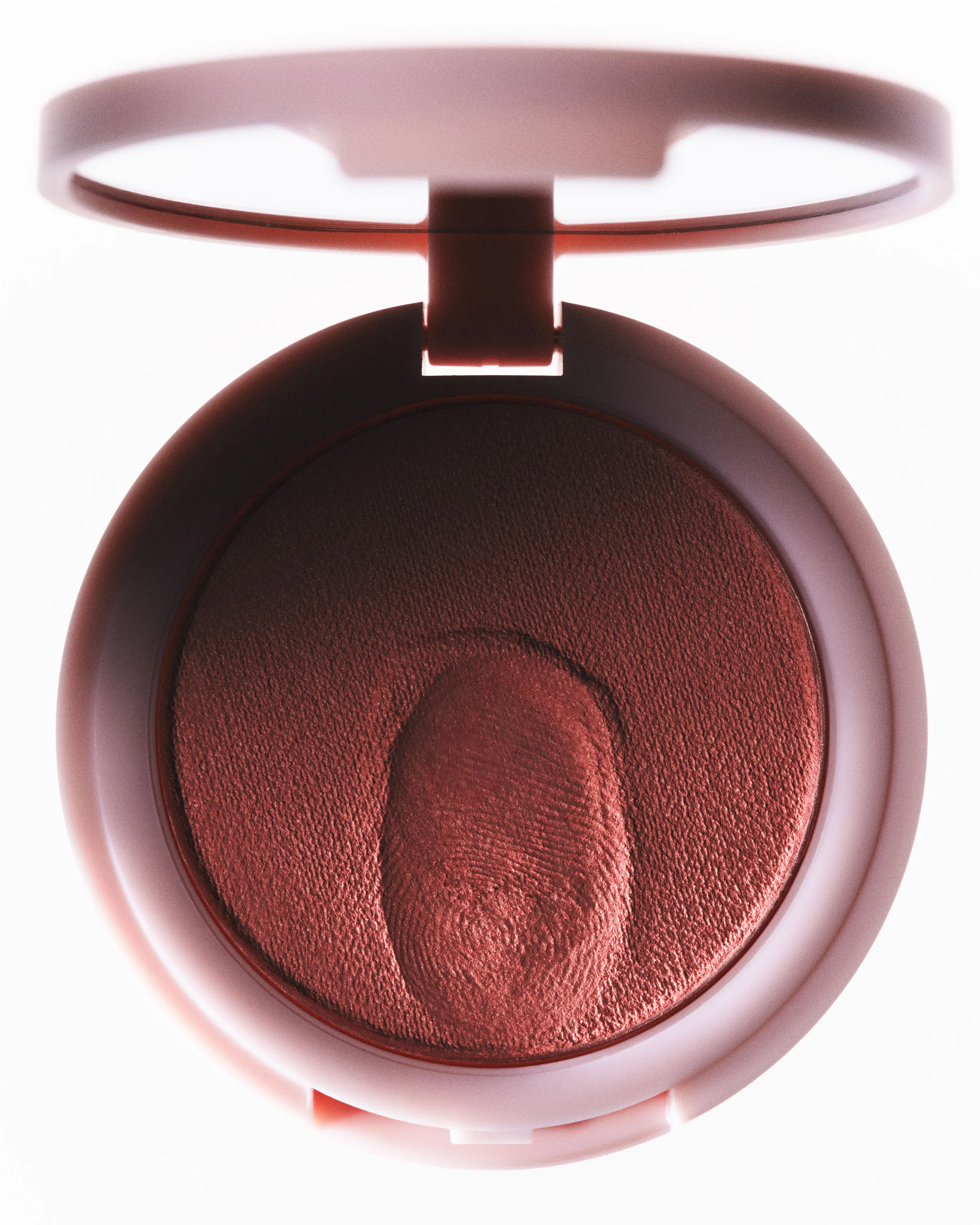 Open pink blush compact with a fingerprint pressed into the rose powder, shot on a pale background, for Kylie Cosmetics.