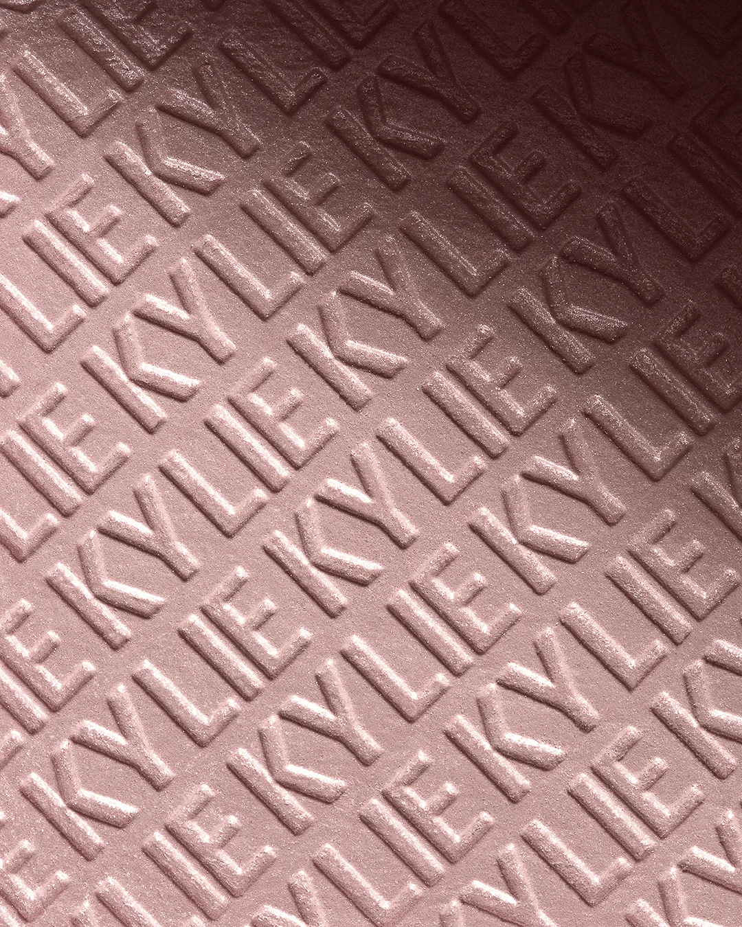 Close-up of pink pressed powder embossed with a repeating KYLIE pattern, for Kylie Cosmetics.