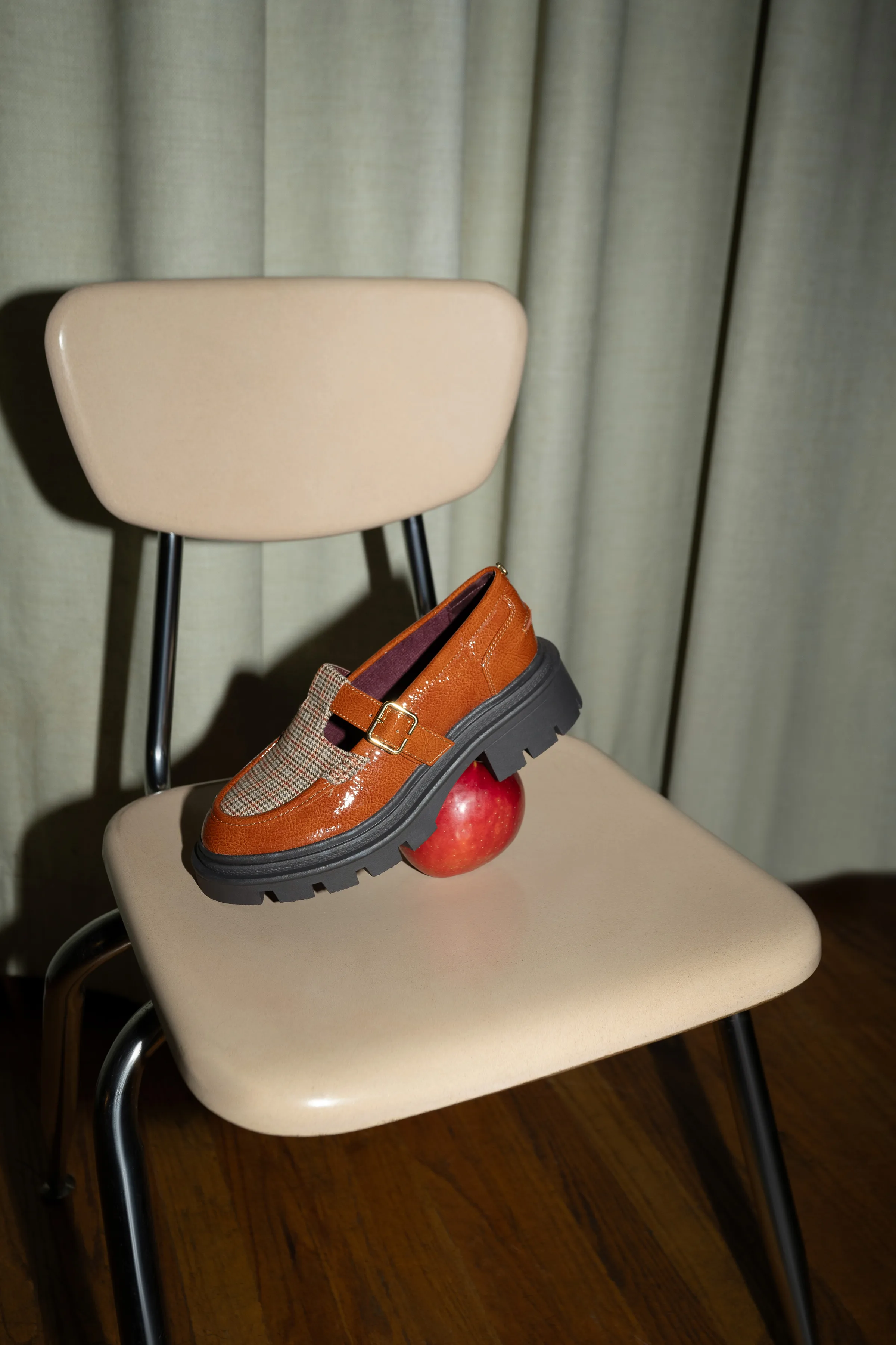 Tan patent lug-sole loafer with plaid panel resting on a red apple atop a beige school chair, for Sam Edelman.