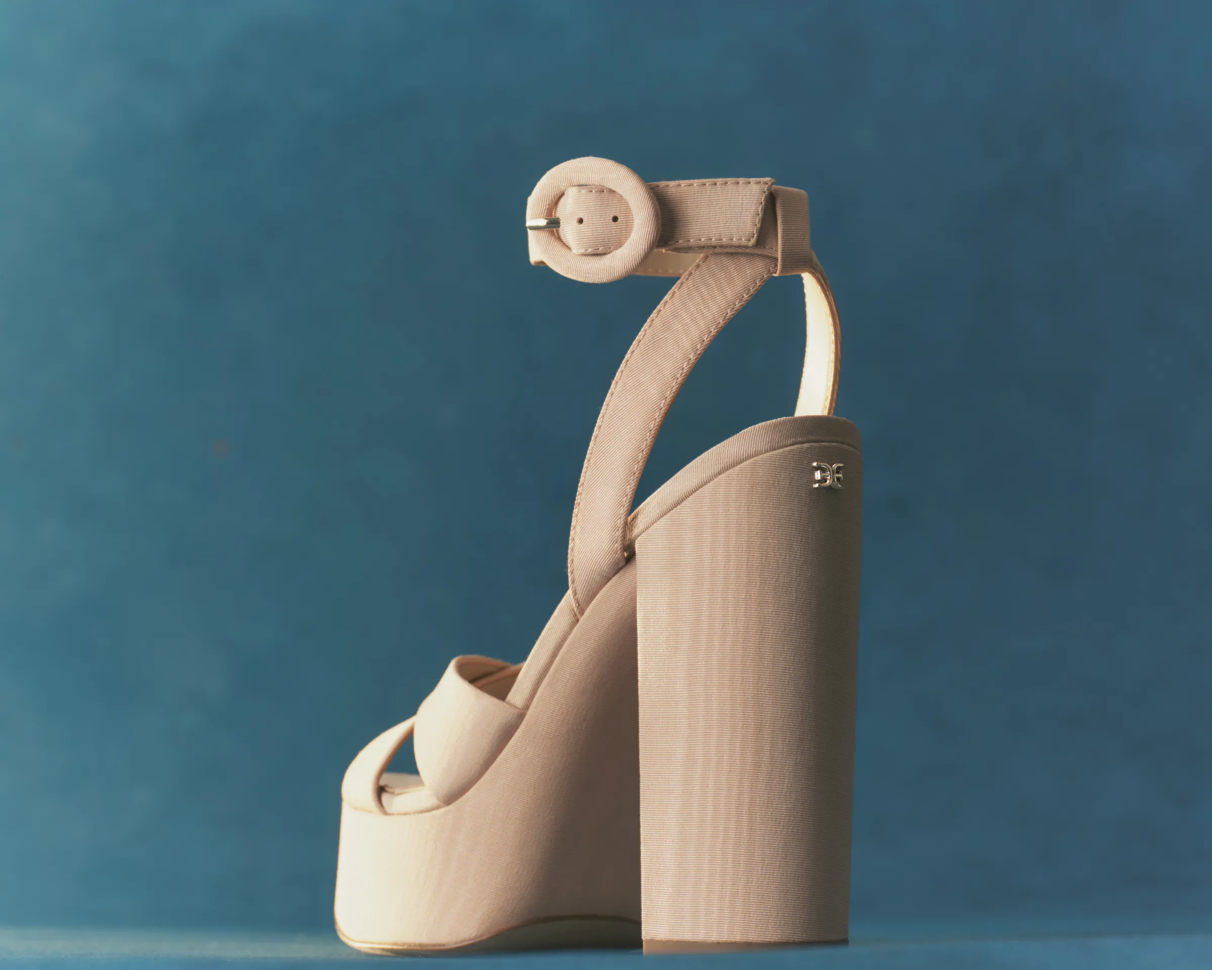 Nude fabric platform sandal with block heel and buckled ankle strap against a teal backdrop, for Sam Edelman.