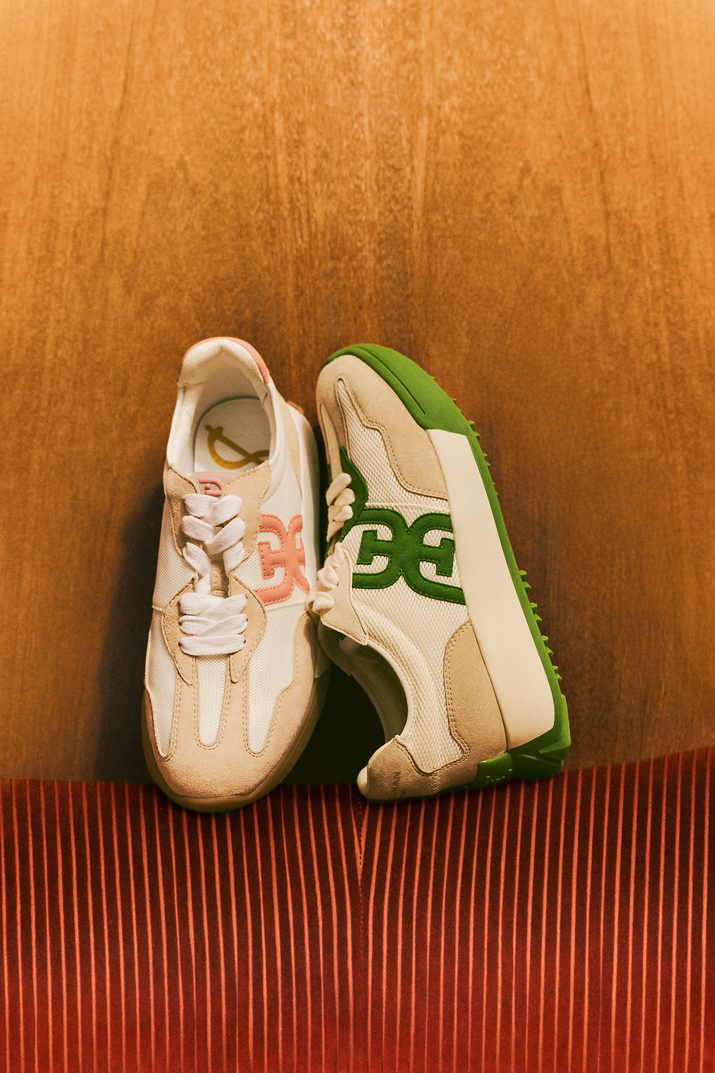 Cream retro sneakers with pink and green double-E logos propped against a wood panel above red corduroy, for Sam Edelman.