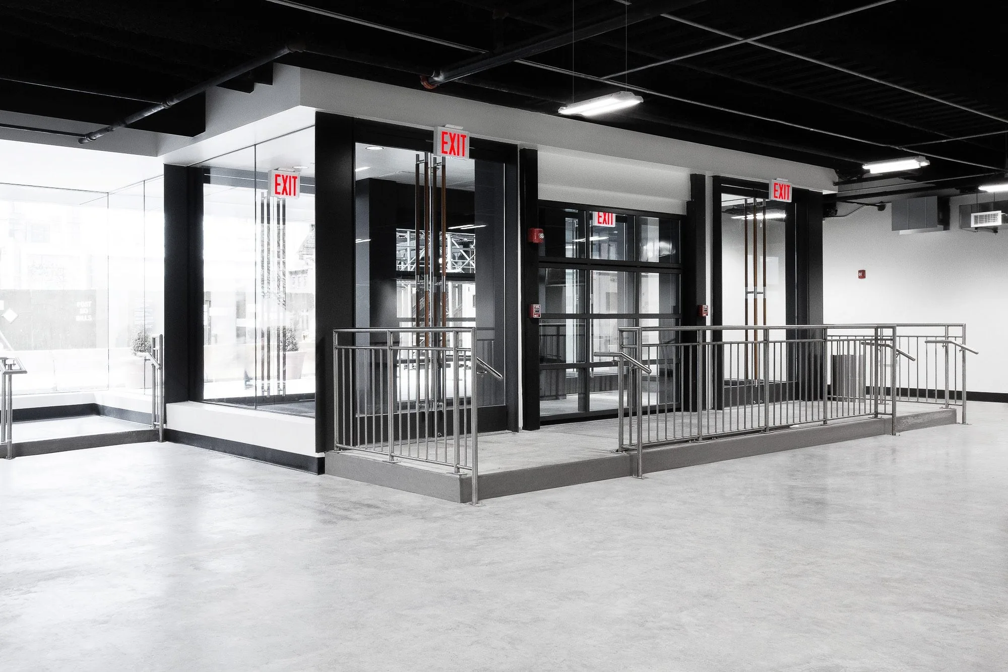 Glass-walled entrance with exit signs, steel-railed ramp and polished grey concrete floor in Slate Studios Studio 2.