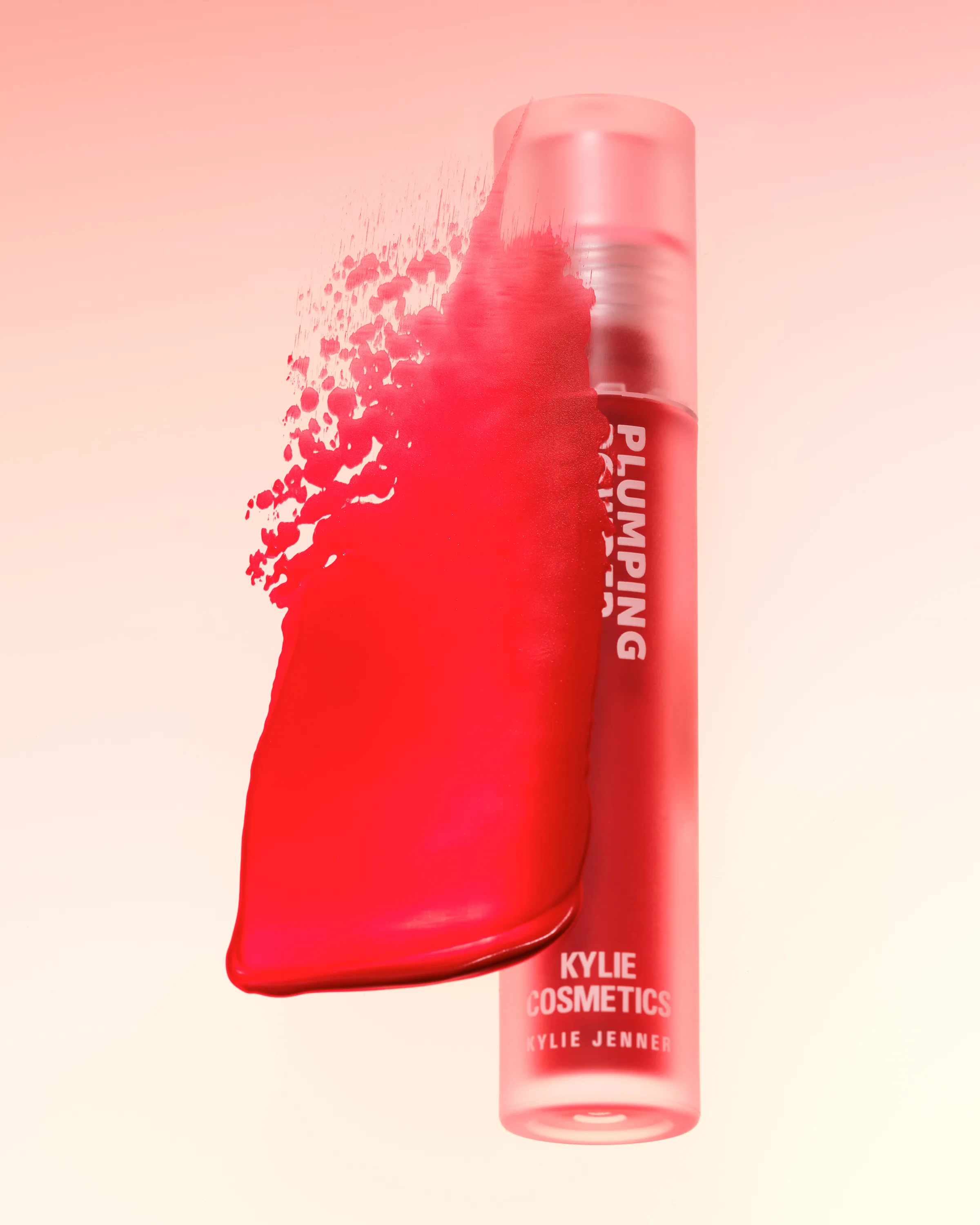CGI render of a frosted red plumping lip gloss tube beside a red product smear on a peach gradient, for Kylie Cosmetics.