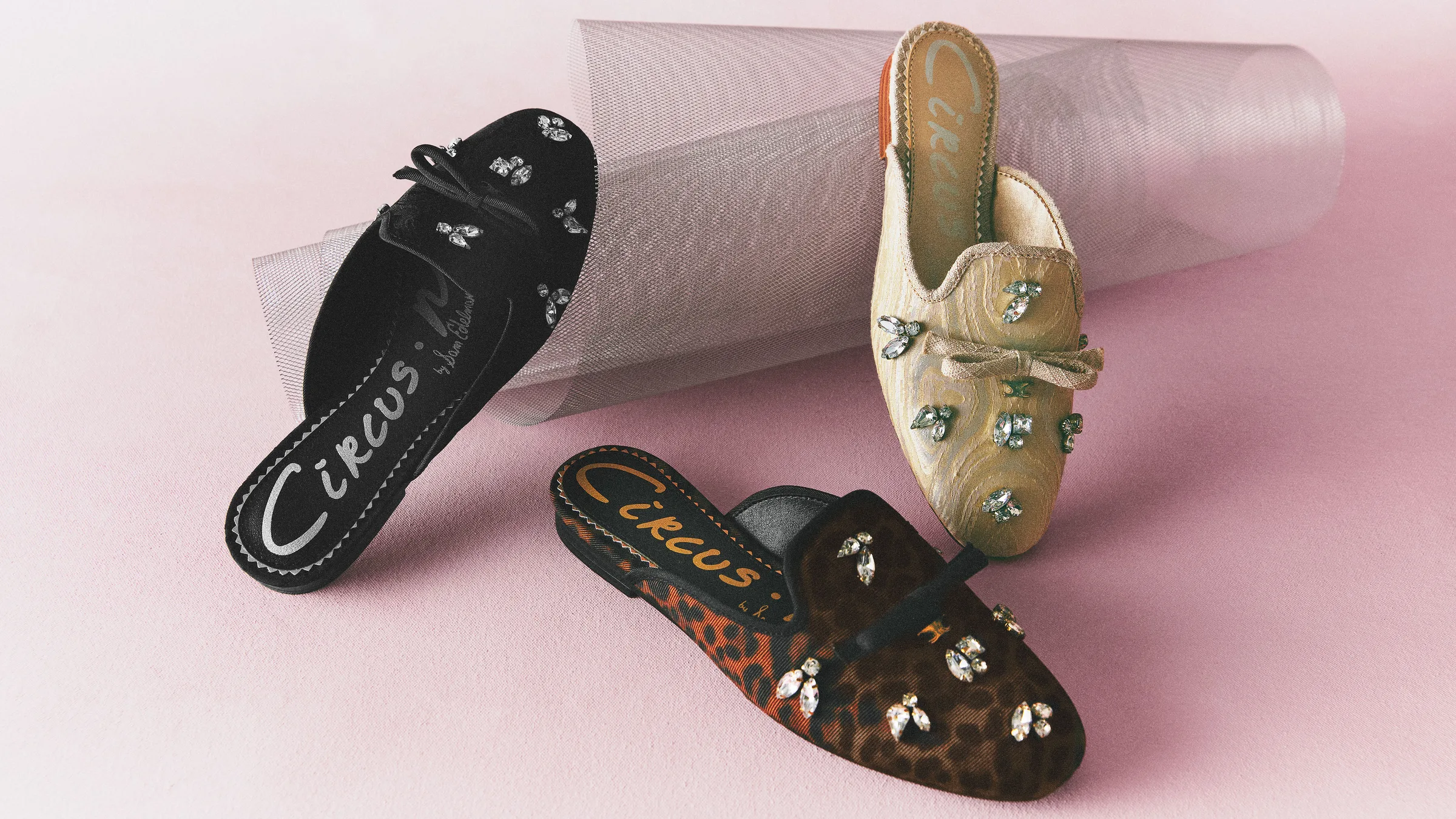 Three jeweled bow mules in black, gold and leopard print with a mesh tube on a pink backdrop, for Circus NY.