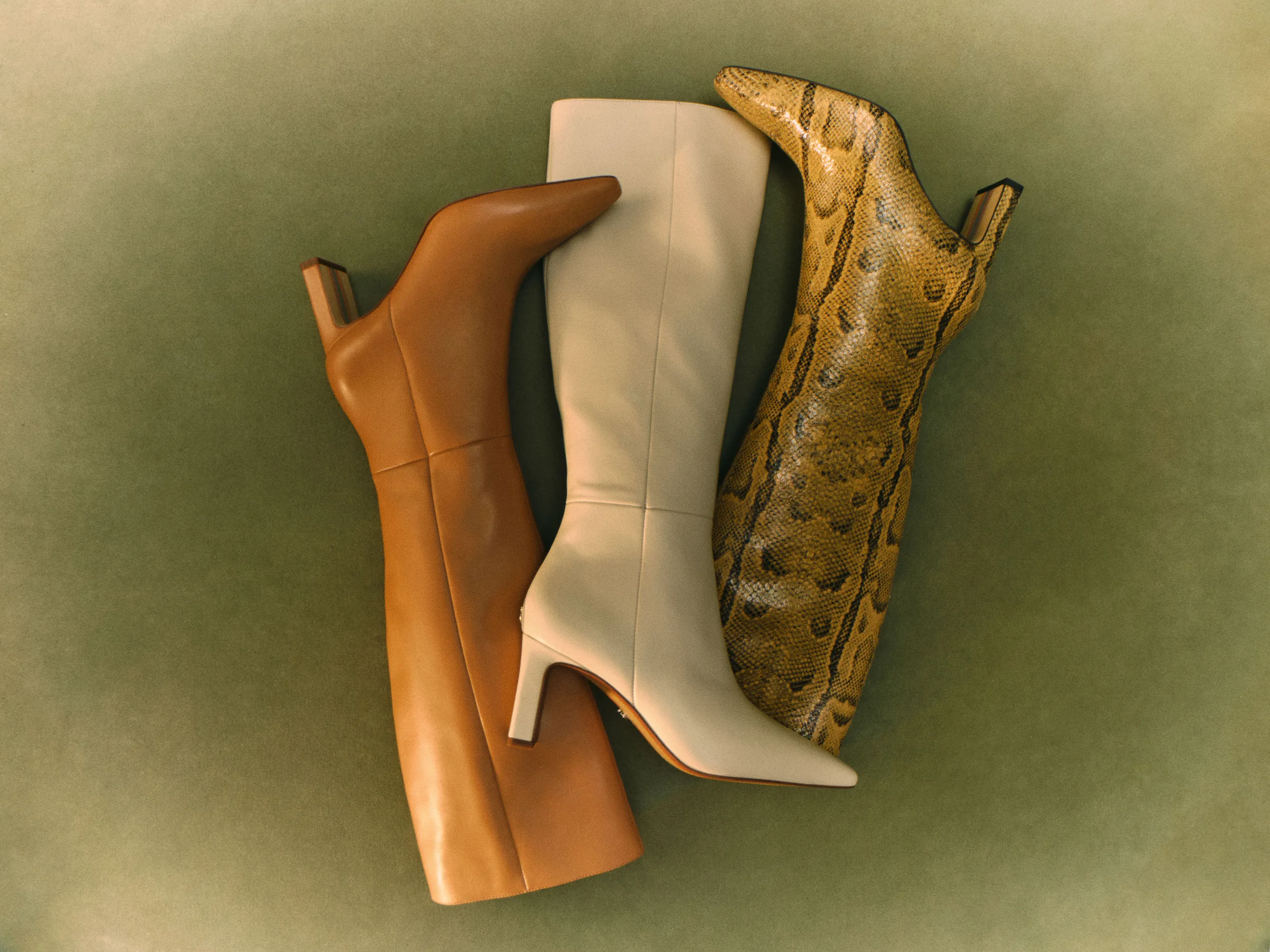 Three knee-high heeled boots in tan leather, ivory leather and golden snakeskin on a green backdrop, for Sam Edelman.
