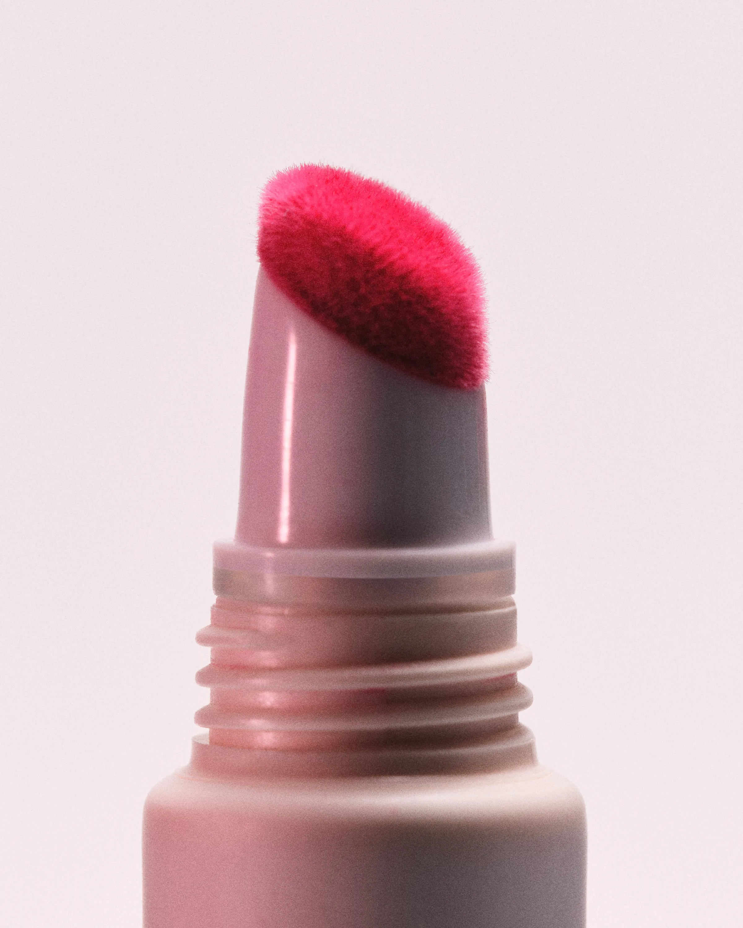 Close-up of a pink lip product tube with a bright pink flocked applicator tip on a pale pink background, for Kylie Cosmetics.