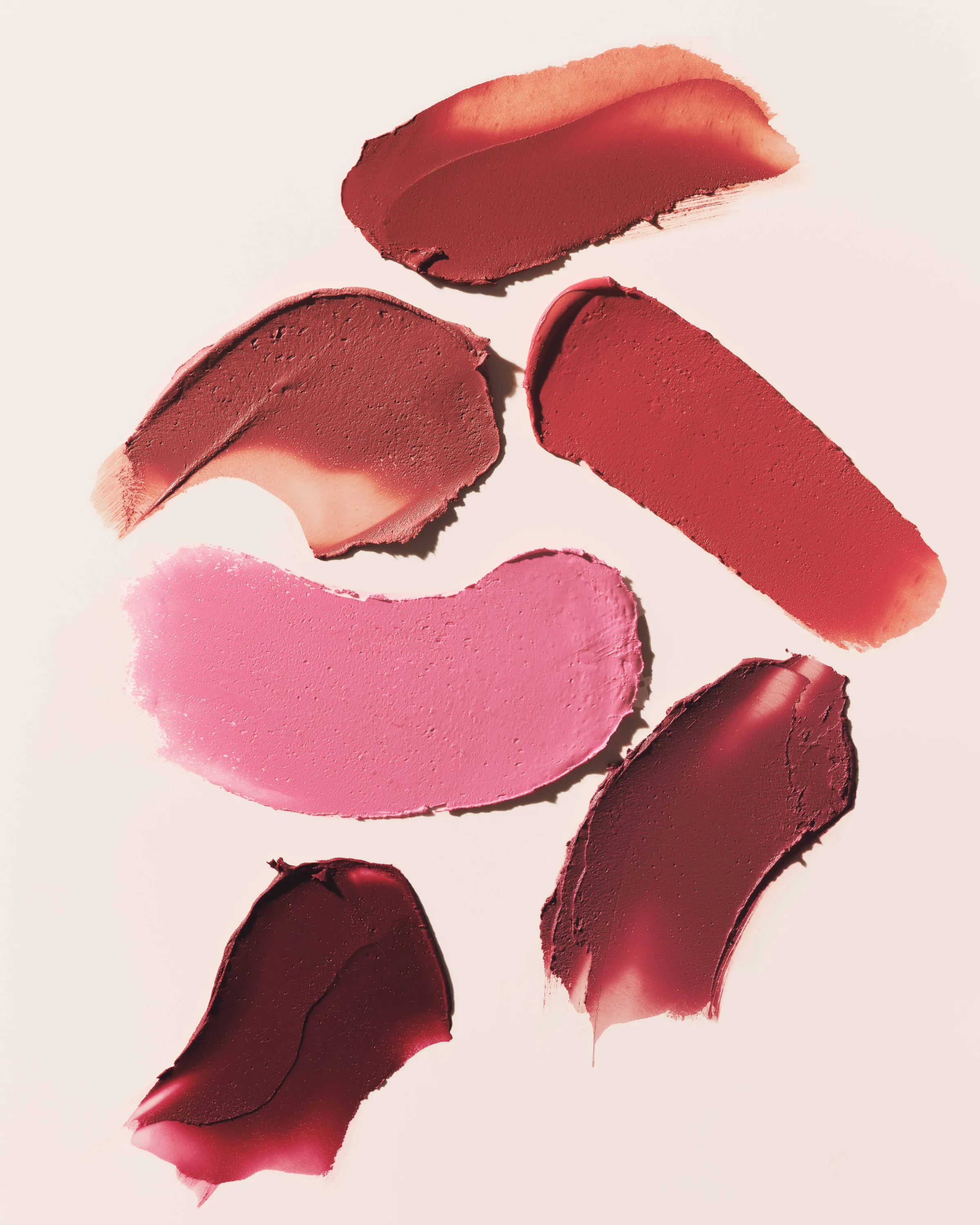 Six lipstick swatches in red, berry, nude and pink smeared across a pale pink background, for Kylie Cosmetics.
