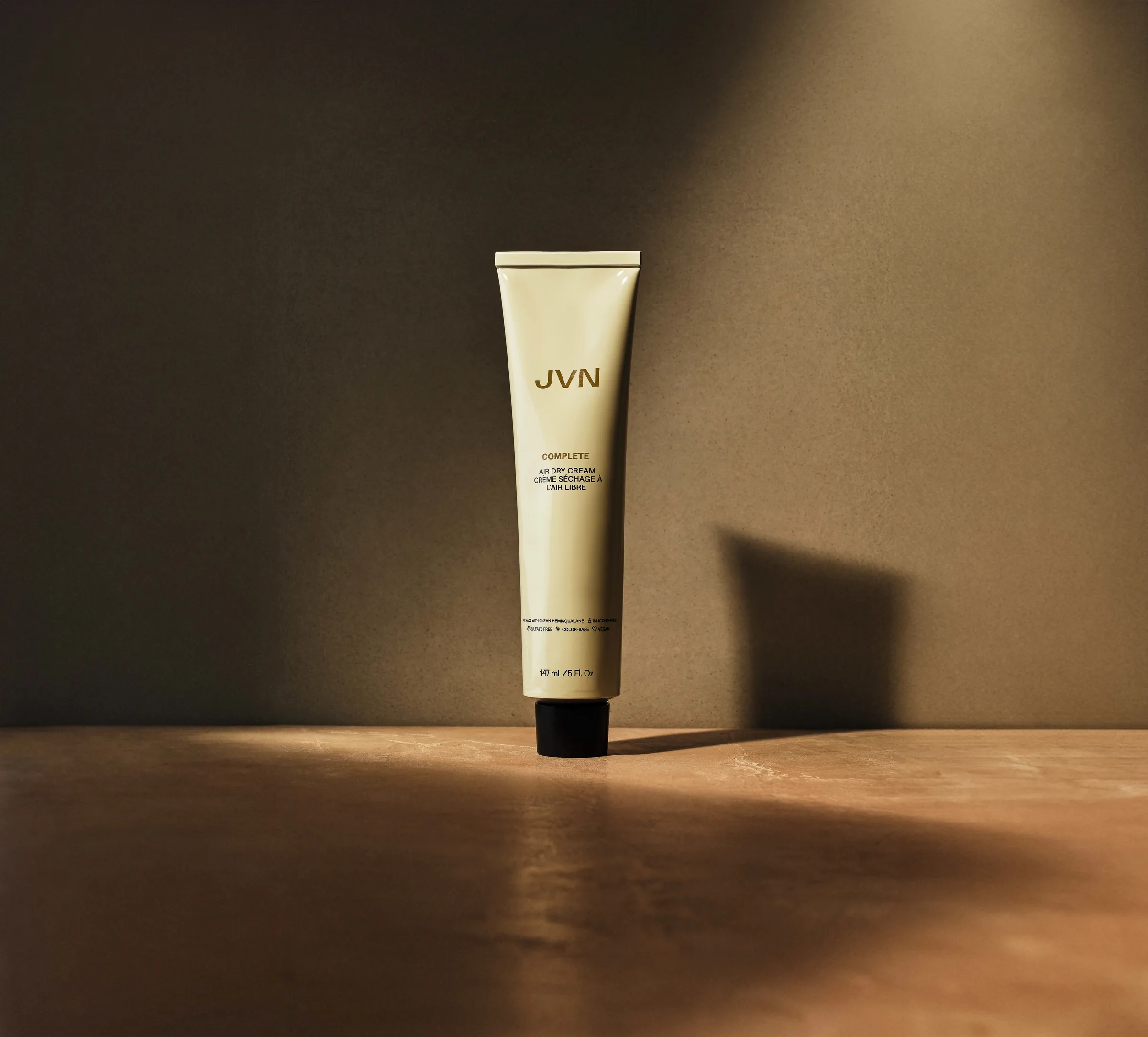 Cream tube of Complete Air Dry Cream standing on a terracotta surface in warm raking light and shadow, for JVN.