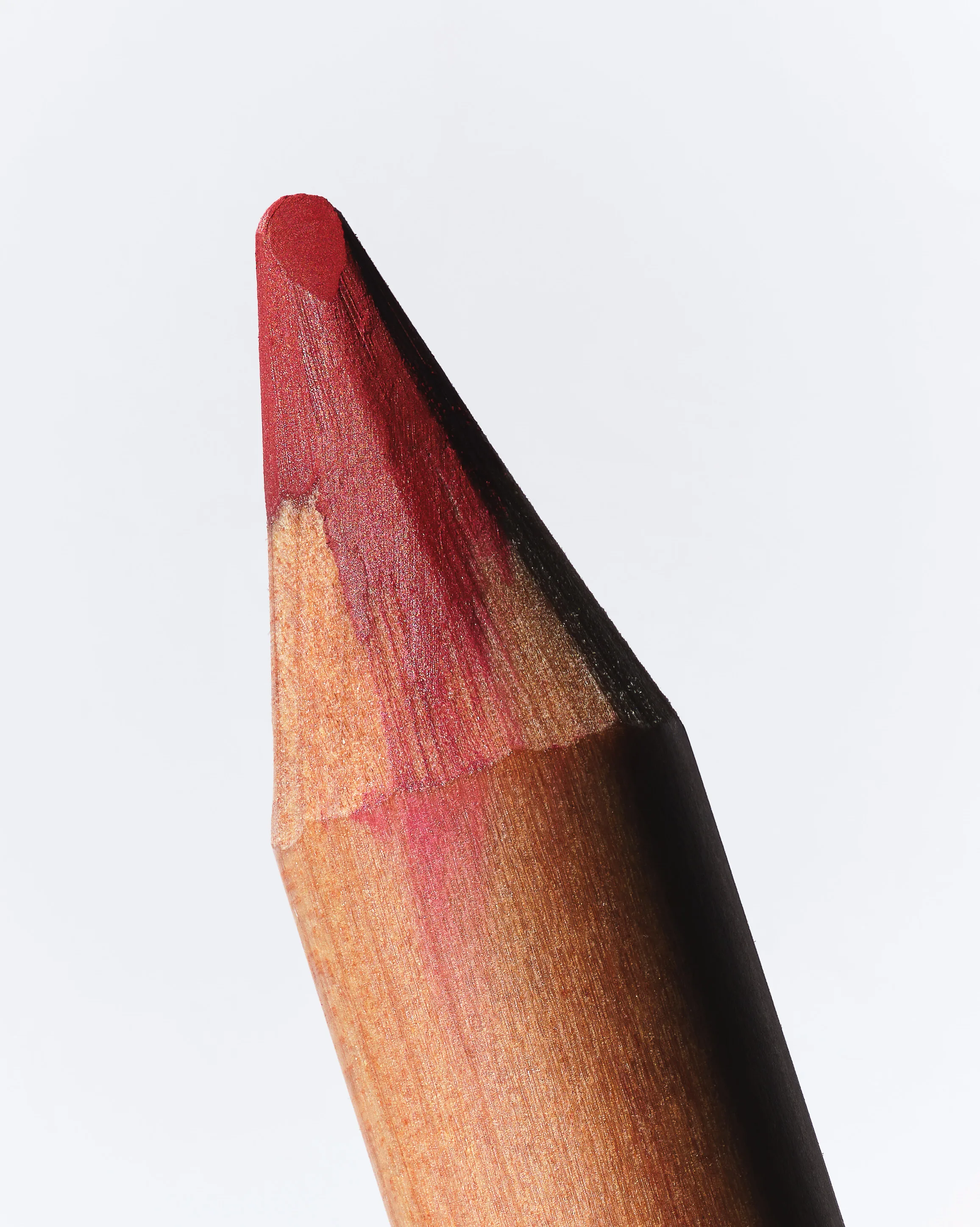 Close-up still life of a sharpened red lip liner pencil tip on a pale grey background, for Kylie Cosmetics.