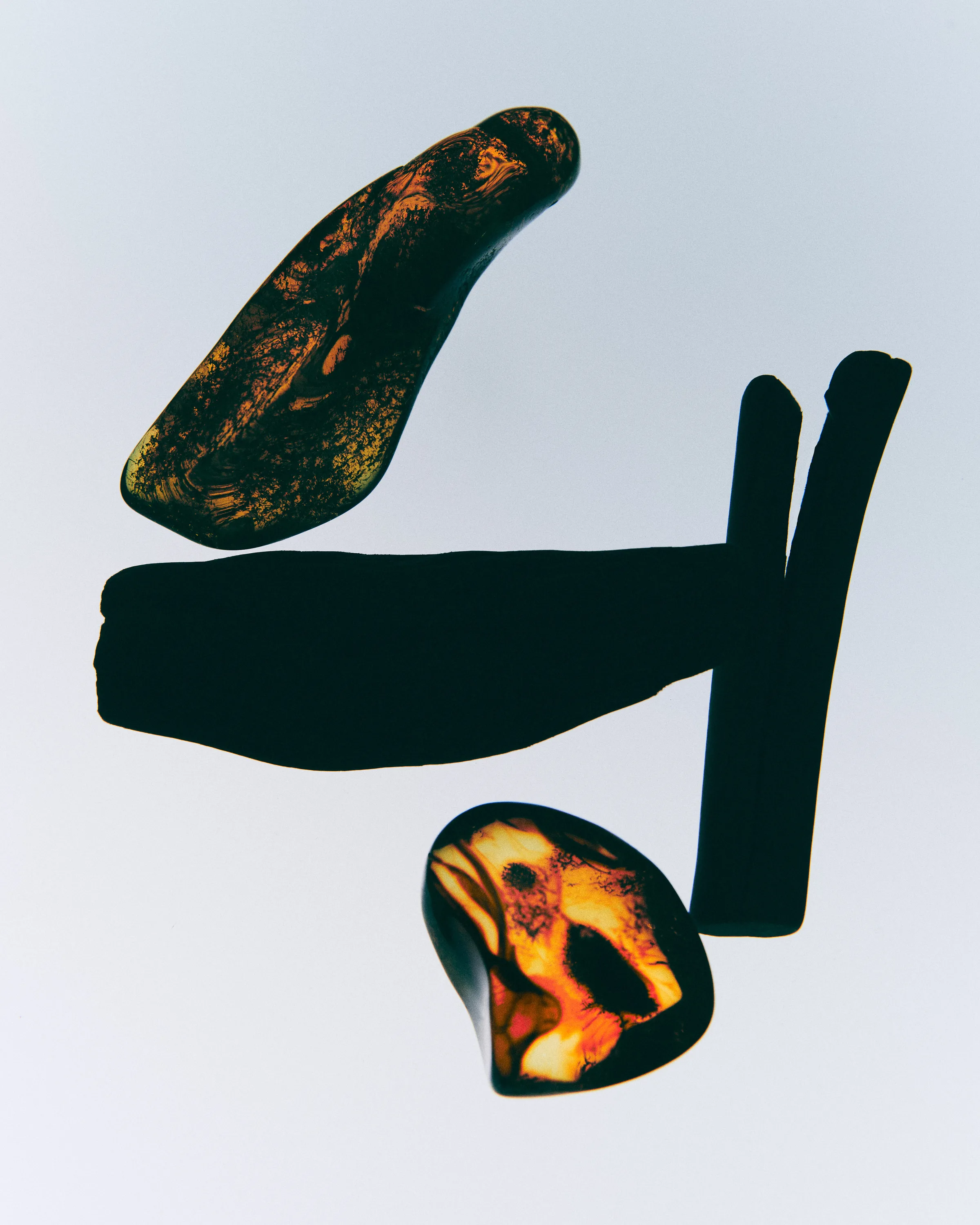 Still life of backlit amber resin pieces and dark wood sticks on a pale grey background, for Kylie Cosmetics.