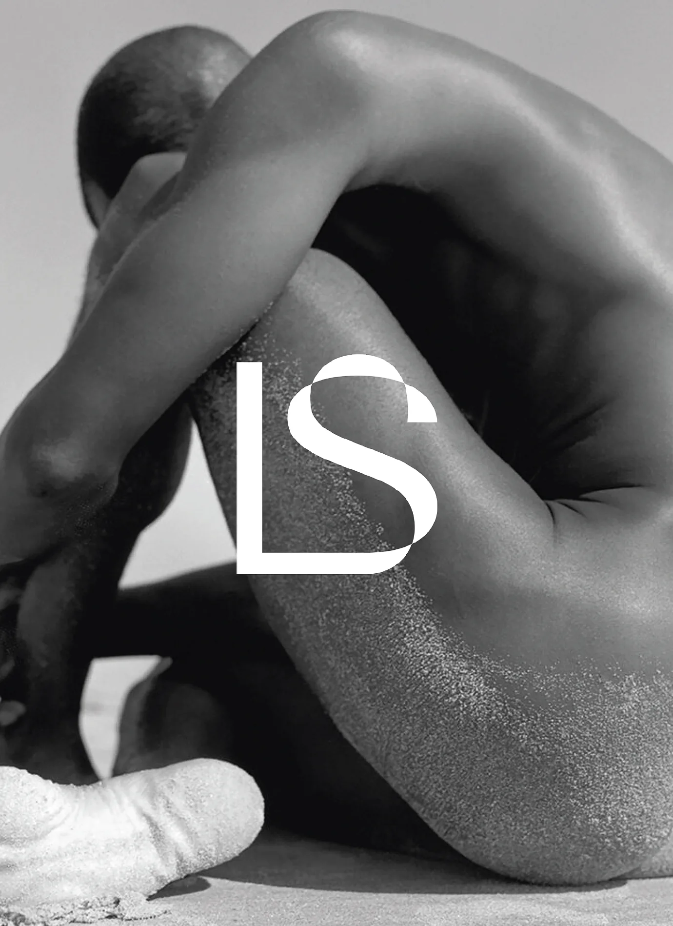 White LS monogram over a black-and-white photo of a curled nude figure on sand, for Lightsaver.