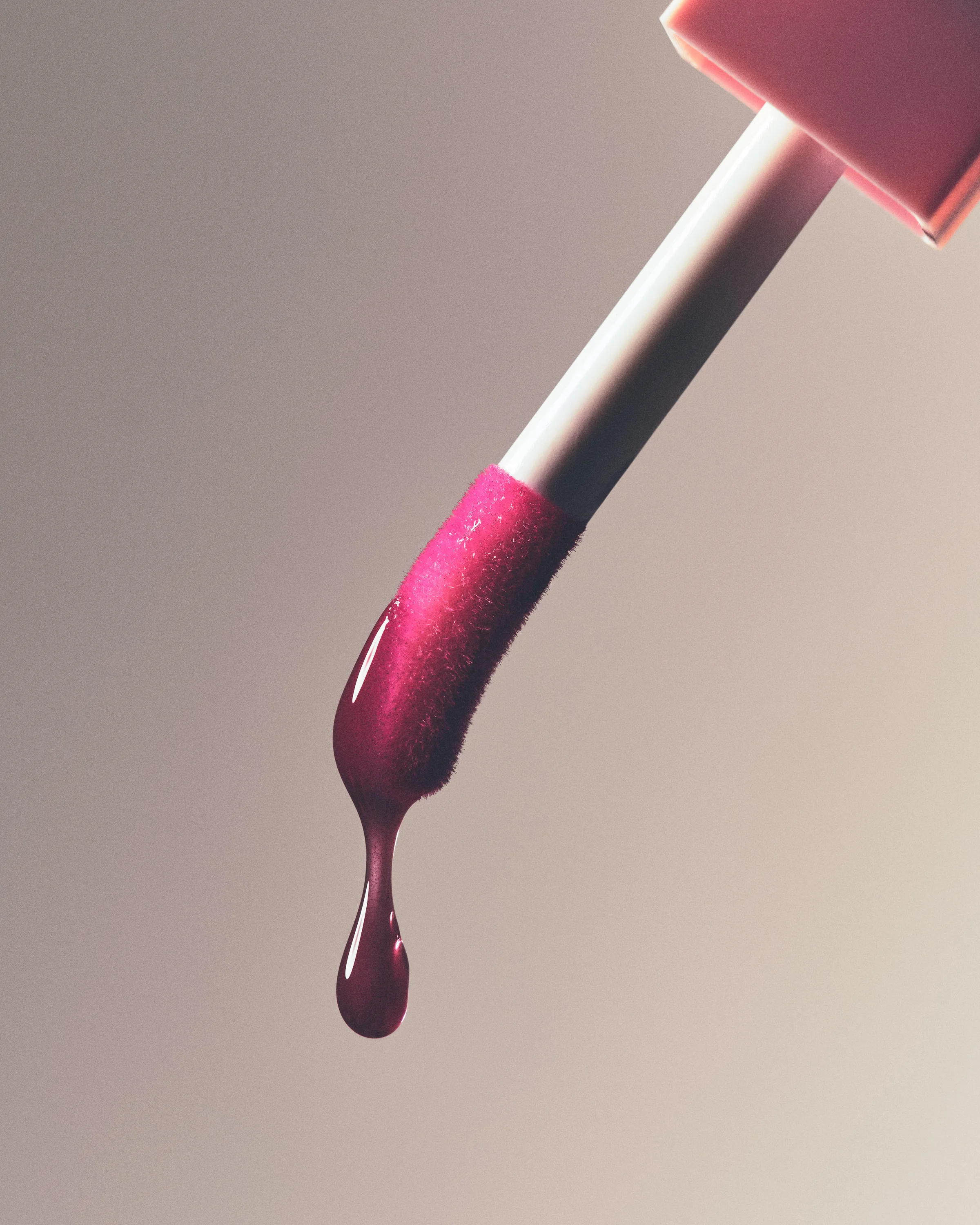 Lip gloss applicator dripping a glossy plum drop against a soft grey background, for Kylie Cosmetics.