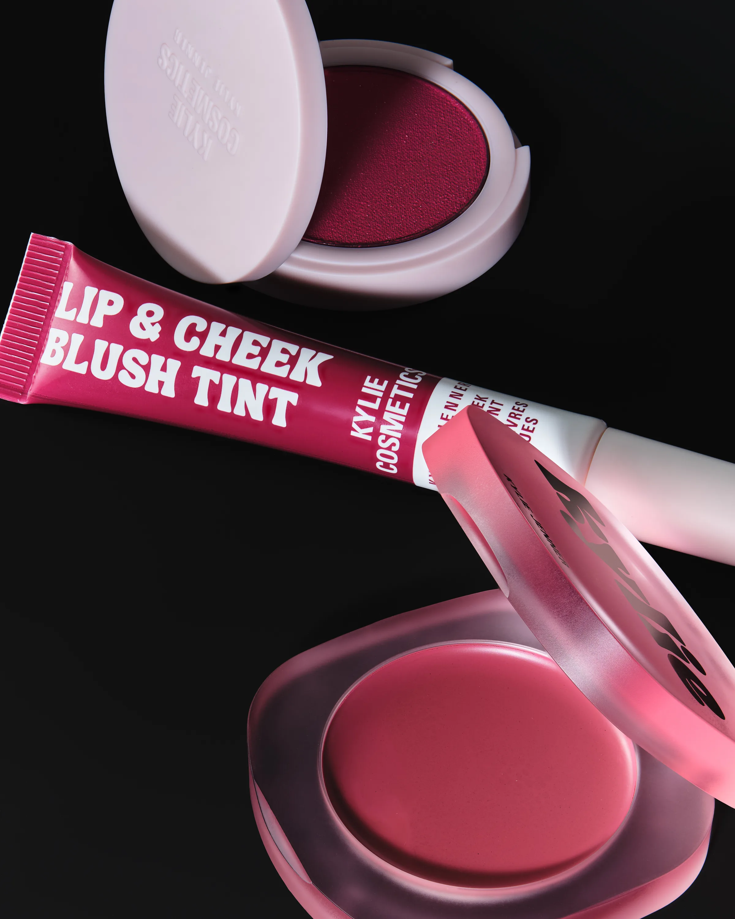 Pink lip and cheek blush tint tube with open berry and rose blush compacts on a black background, for Kylie Cosmetics.
