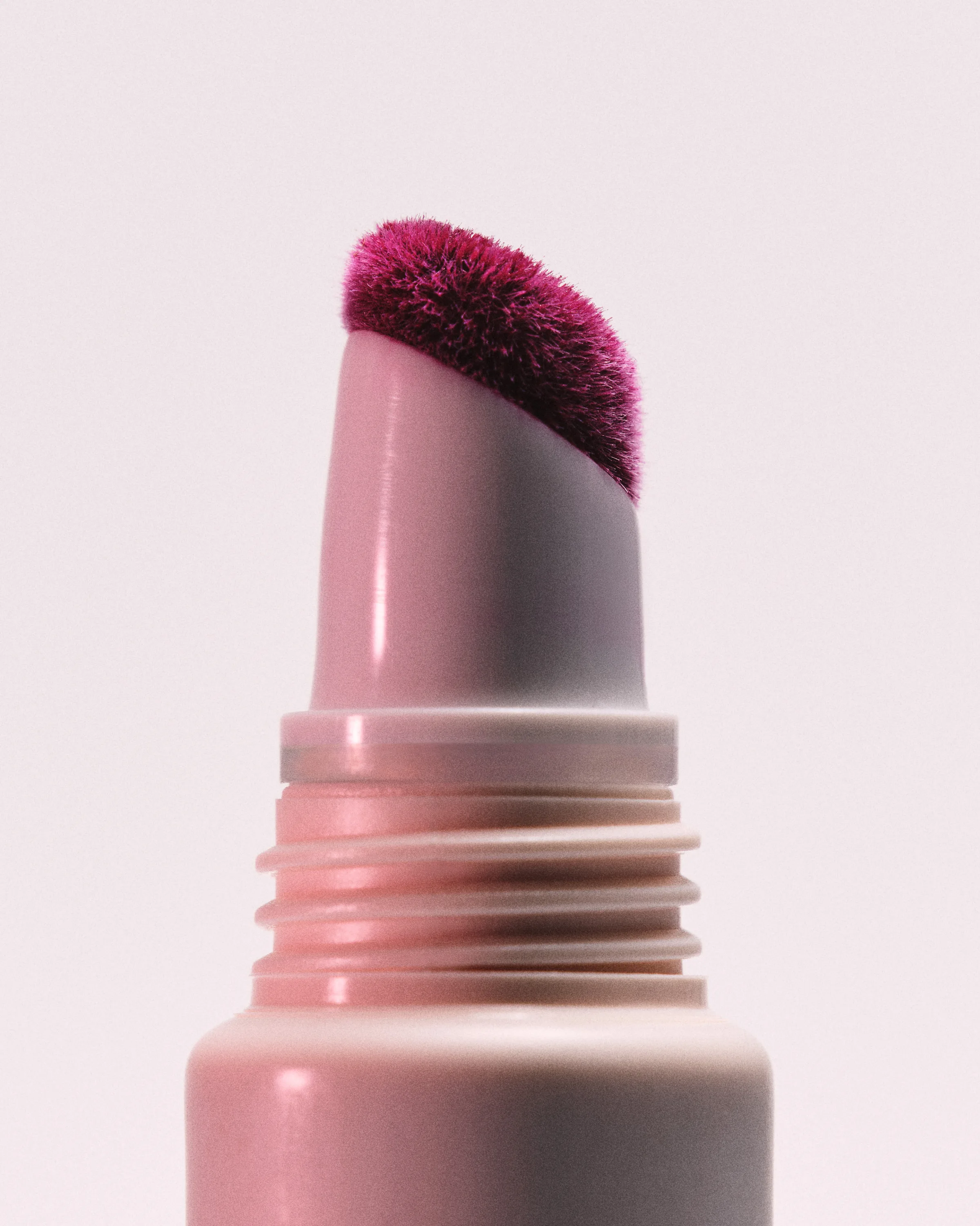 Close-up of a pink tube with a berry-stained angled sponge applicator on a pale pink background, for Kylie Cosmetics.