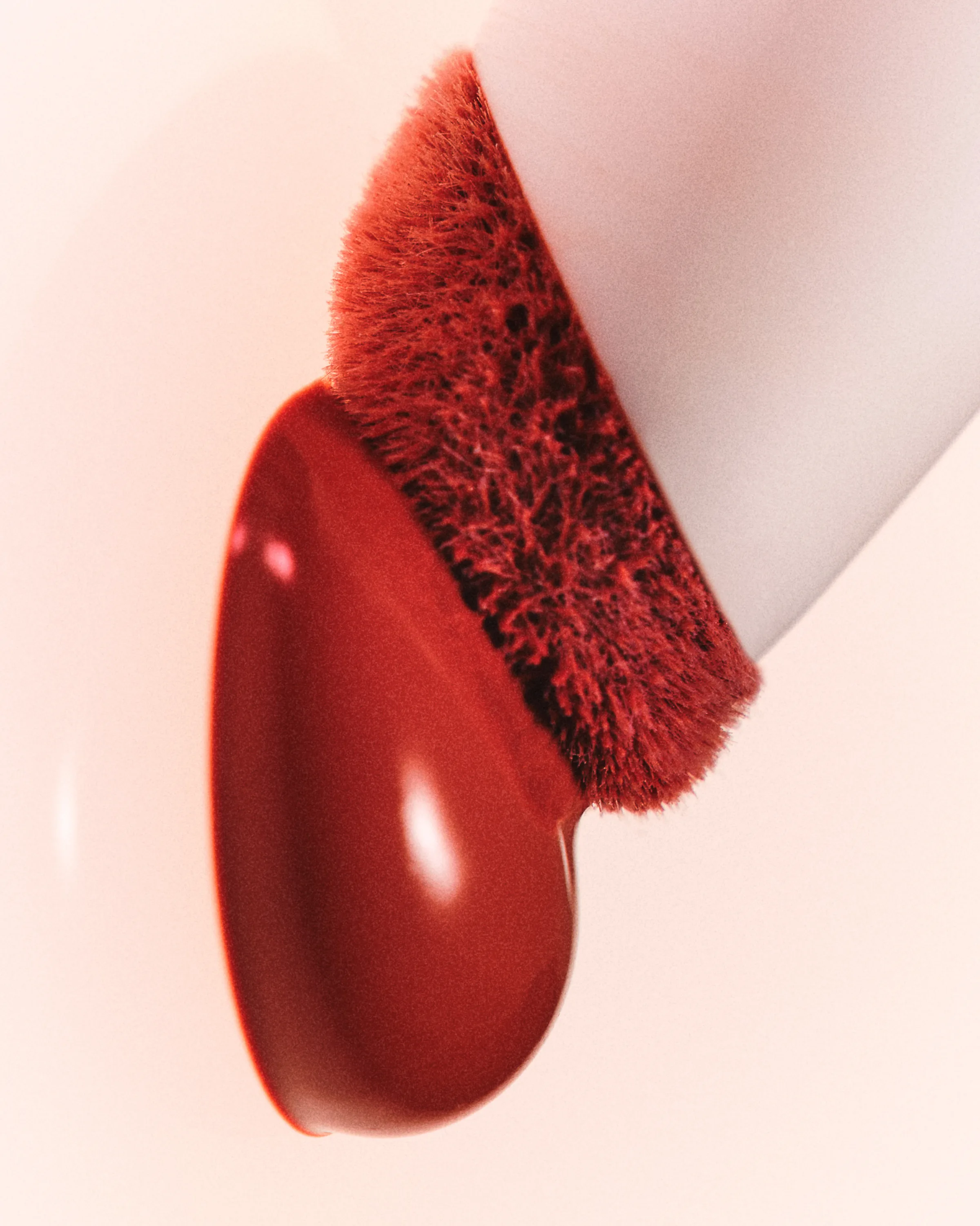Close-up of a glossy red lip product drop on a red flocked applicator against a soft pink background, for Kylie Cosmetics.