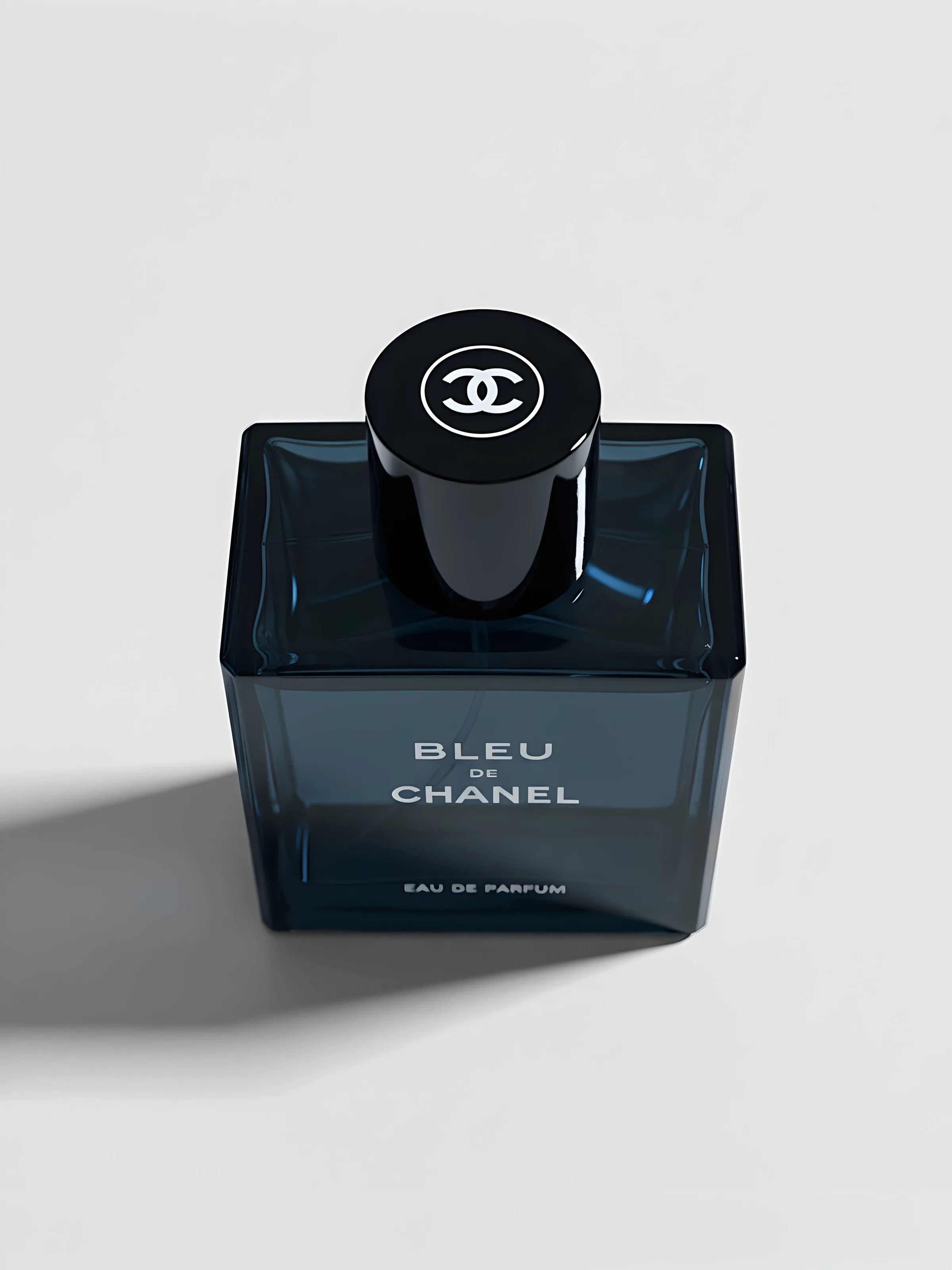 AI image of a dark blue Bleu de Chanel eau de parfum bottle with black cap on a white surface, casting a long shadow. Chanel AI Concept.