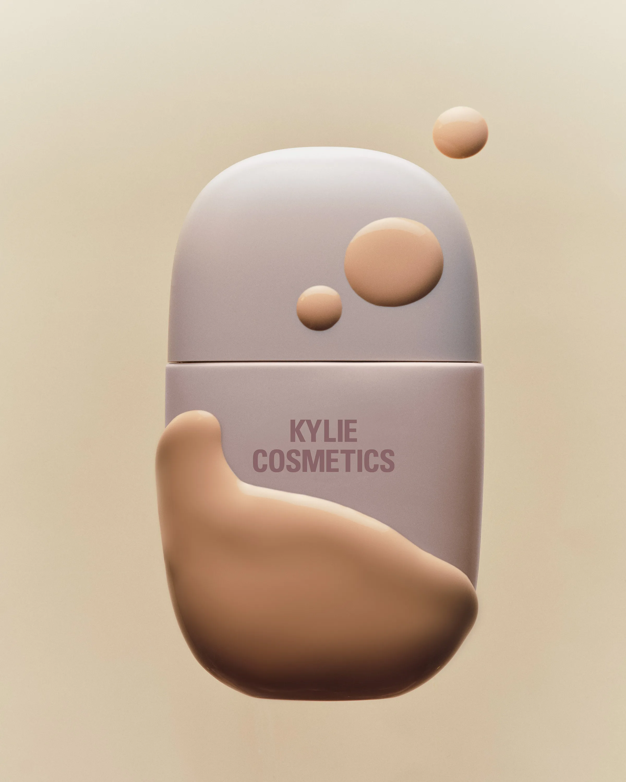 Mauve foundation bottle with smeared and dotted beige foundation swatches on a cream background, for Kylie Cosmetics.