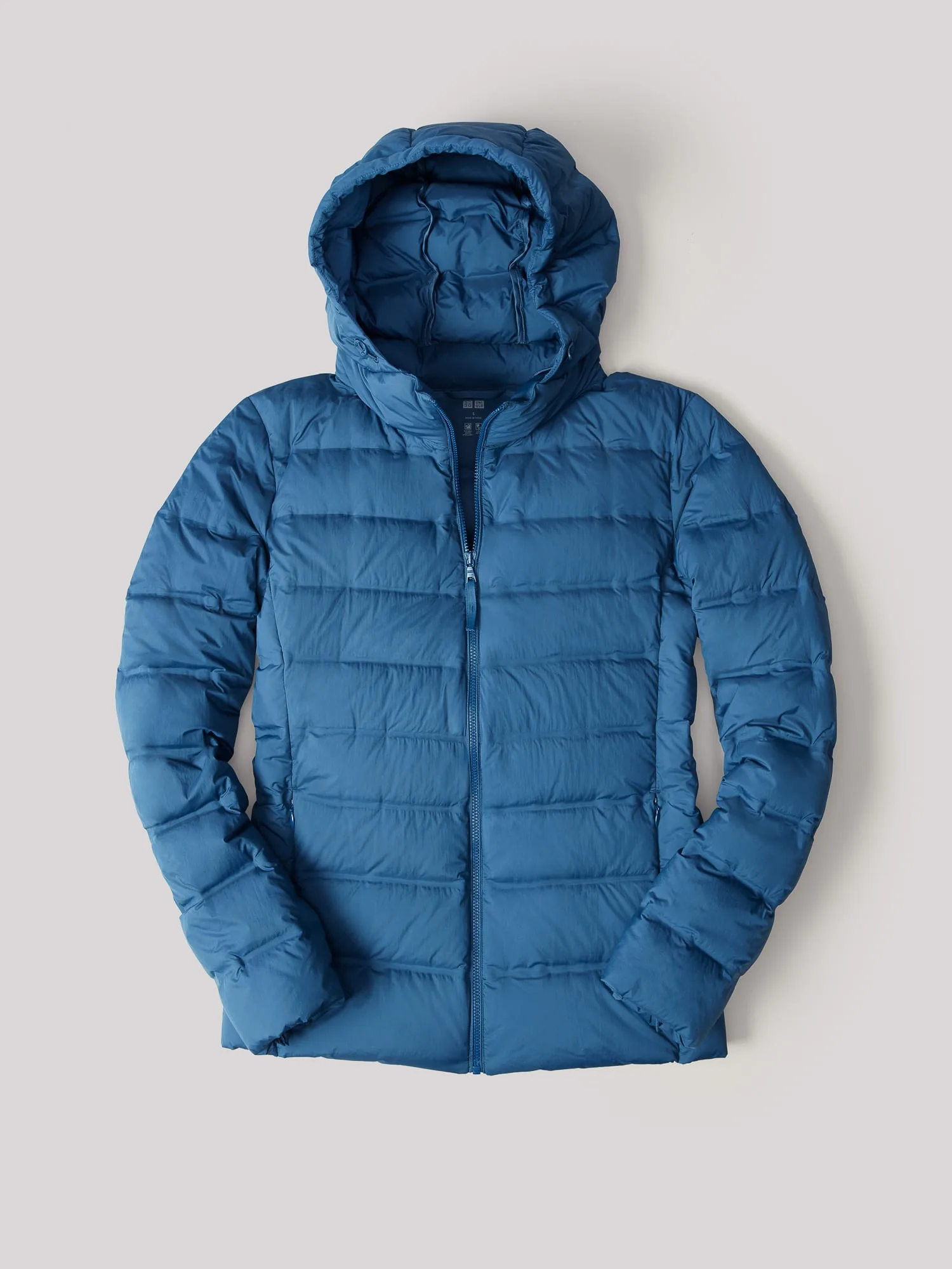 Blue quilted hooded puffer jacket laid flat on a light grey background, for Uniqlo.