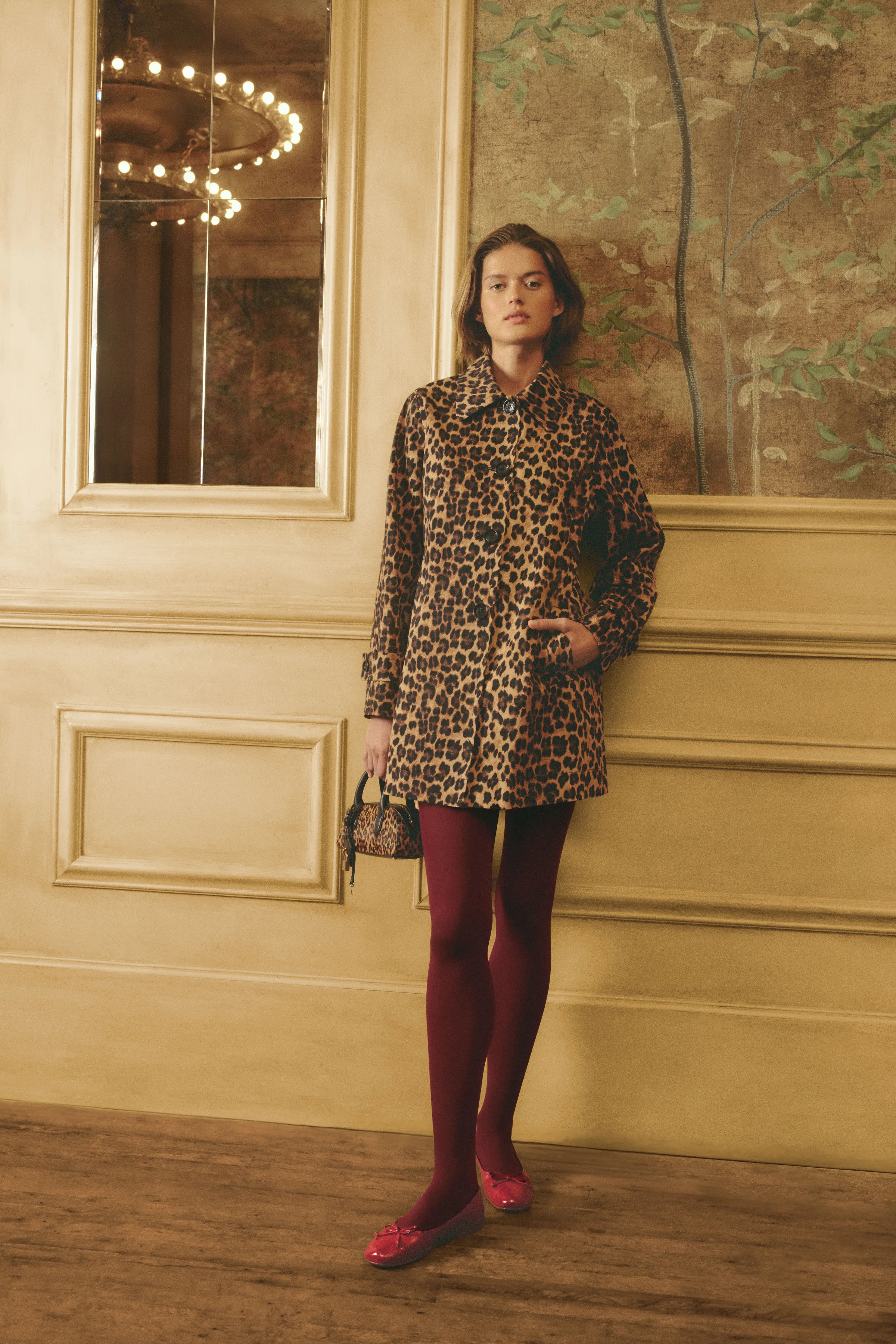 Model in a leopard print coat, burgundy tights and red bow flats in a gilded panelled room, for Sam Edelman.