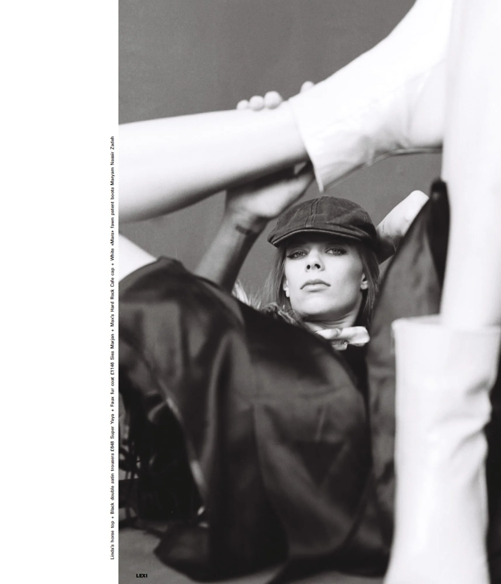 Black and white editorial of a model in a newsboy cap and satin trousers reclining beneath raised legs, for Marfa Journal.