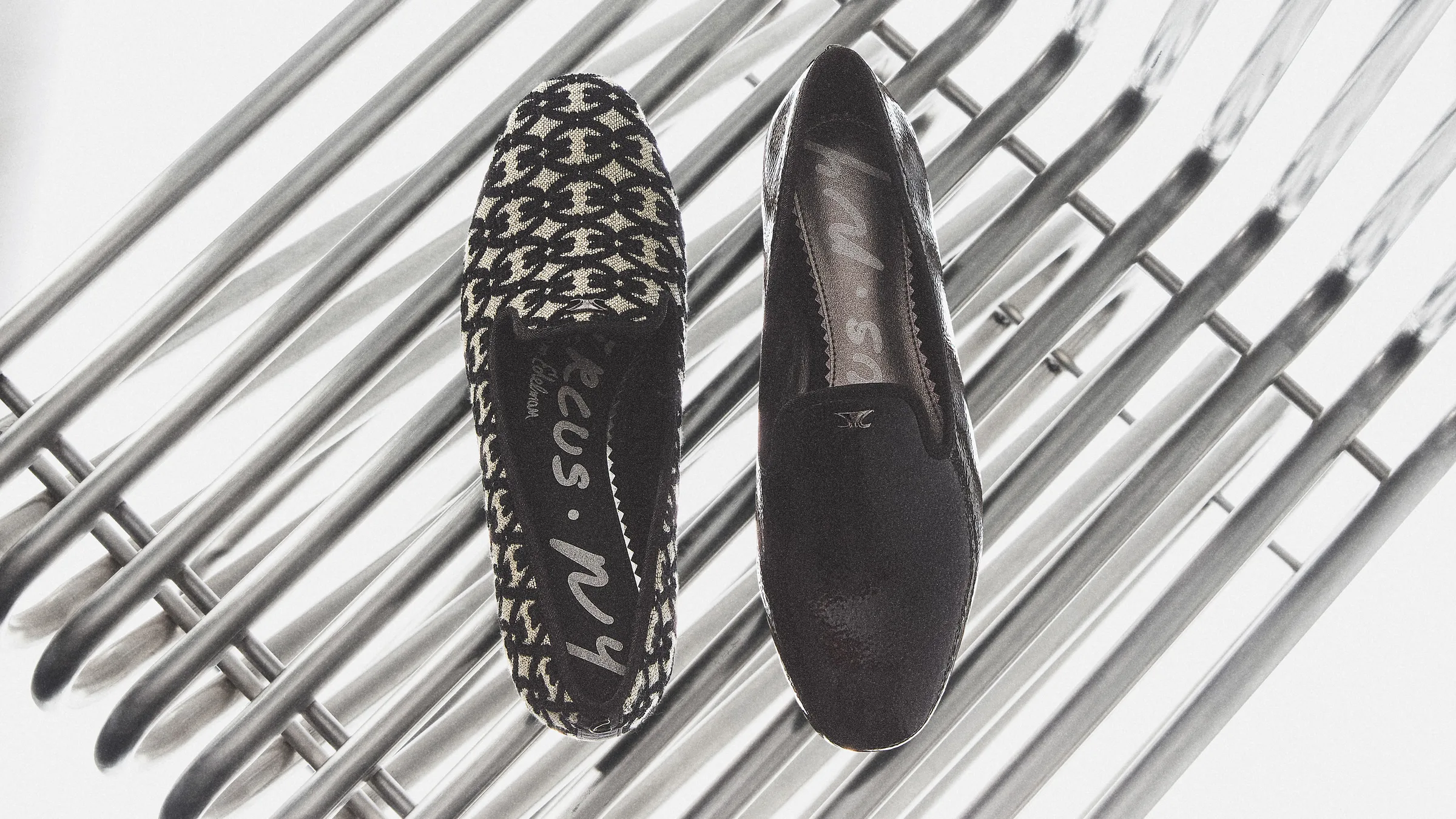 Pair of Tiffany smoking loafers, one black-and-natural patterned, one black, on a chrome rack, for Circus NY.