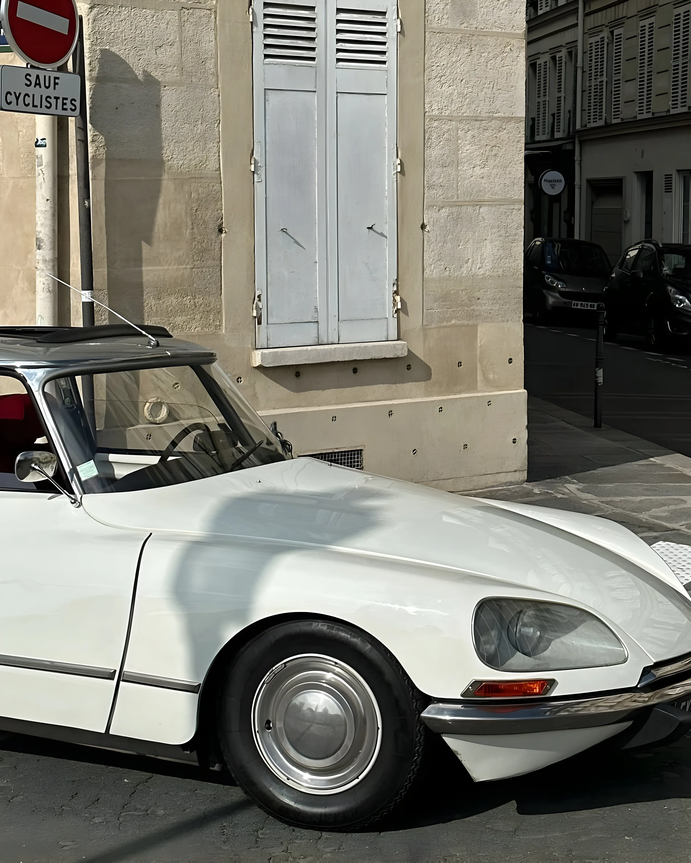 Vintage white Citroën DS parked on a Paris street corner beside a stone building with grey shutters.