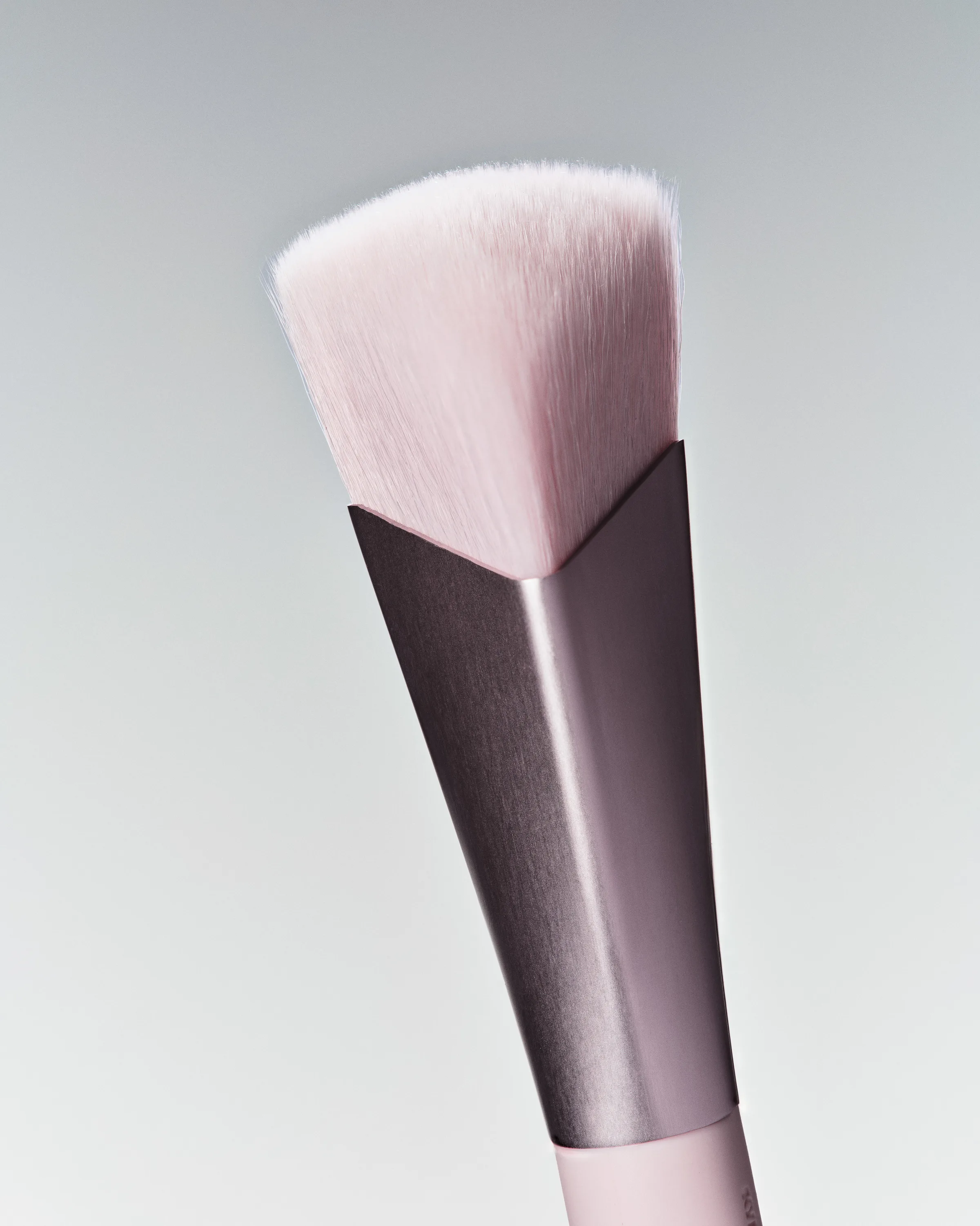 Angled pink makeup brush with a brushed metal ferrule against a soft grey backdrop, for Kylie Cosmetics.