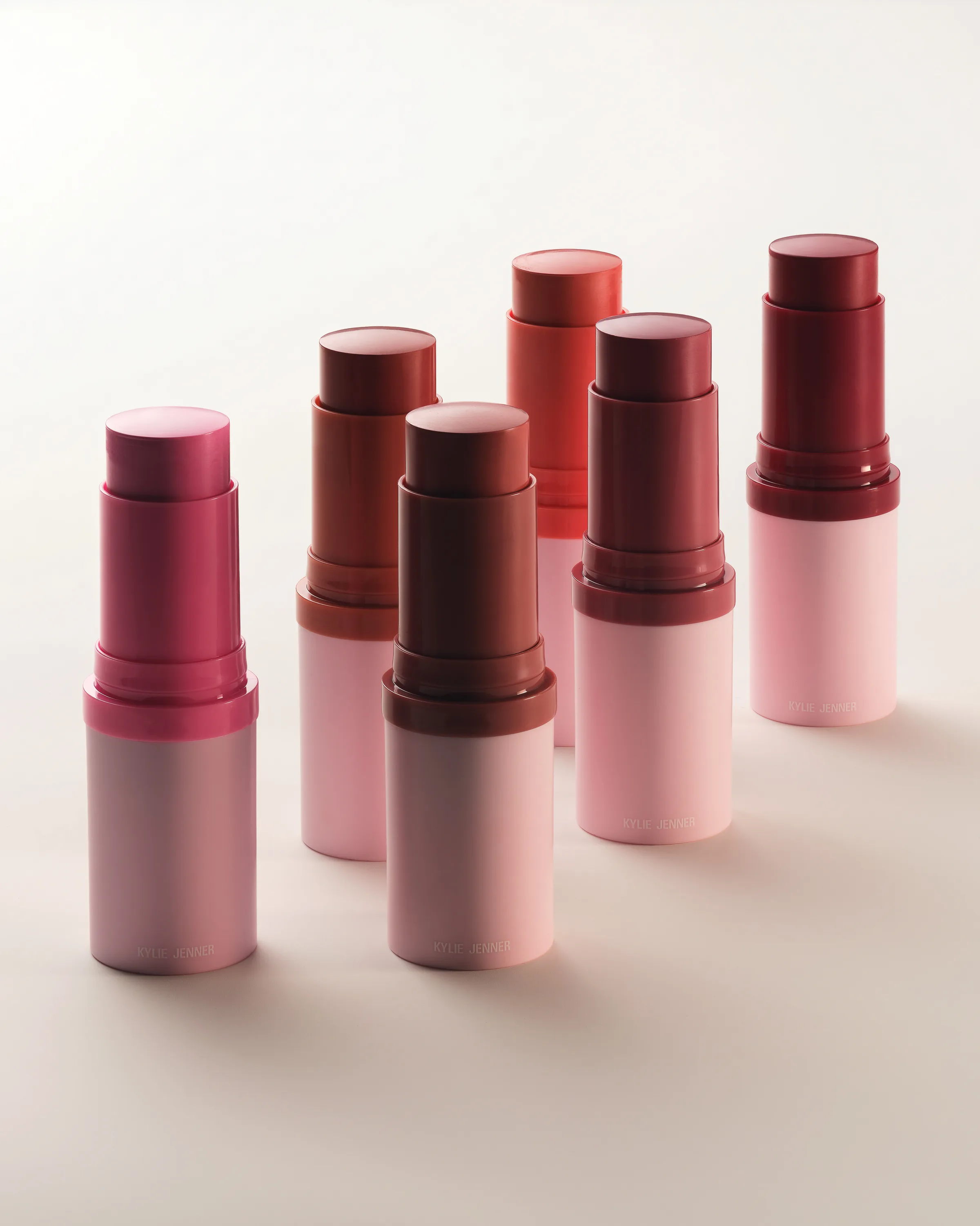 Six uncapped blush sticks in pink, red and berry shades with pale pink tubes on a cream backdrop, for Kylie Cosmetics.