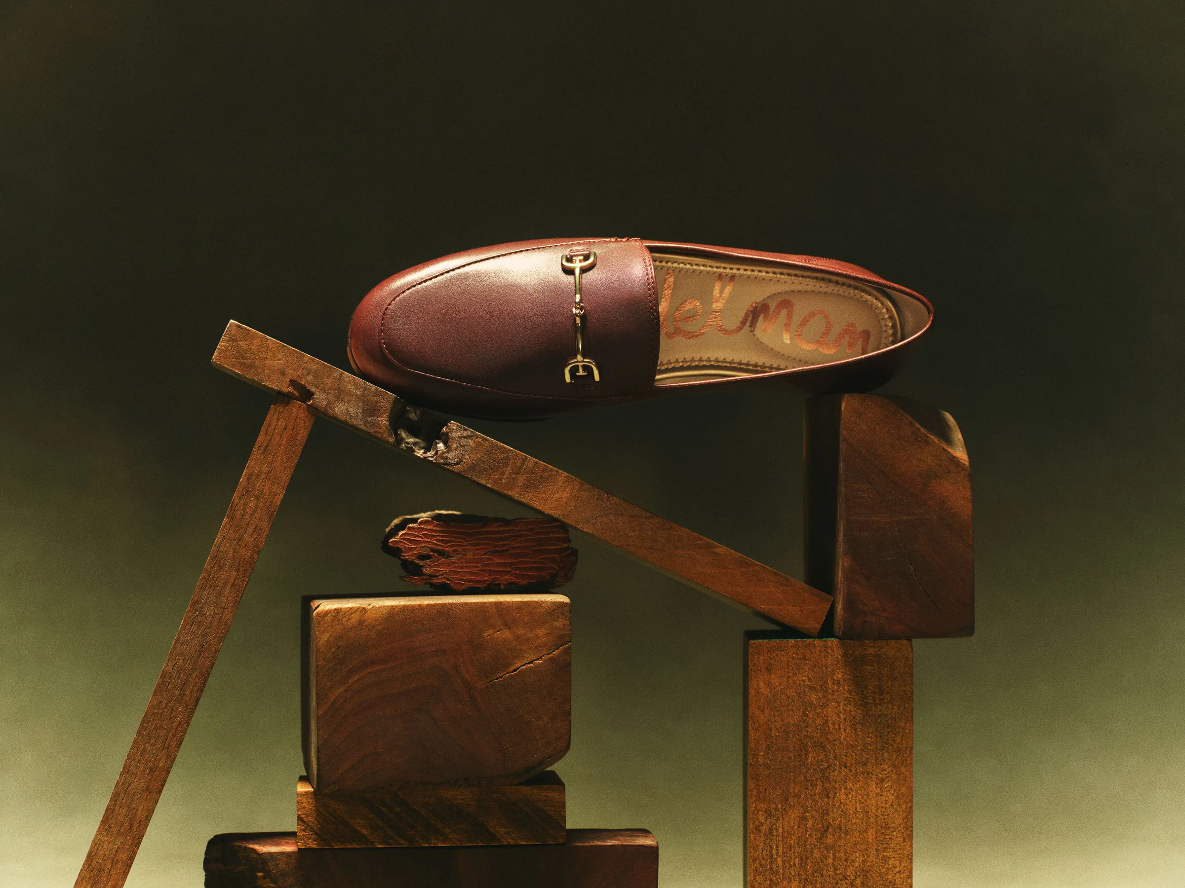 Burgundy leather horsebit loafer balanced on stacked wooden blocks against a dark green backdrop, for Sam Edelman.