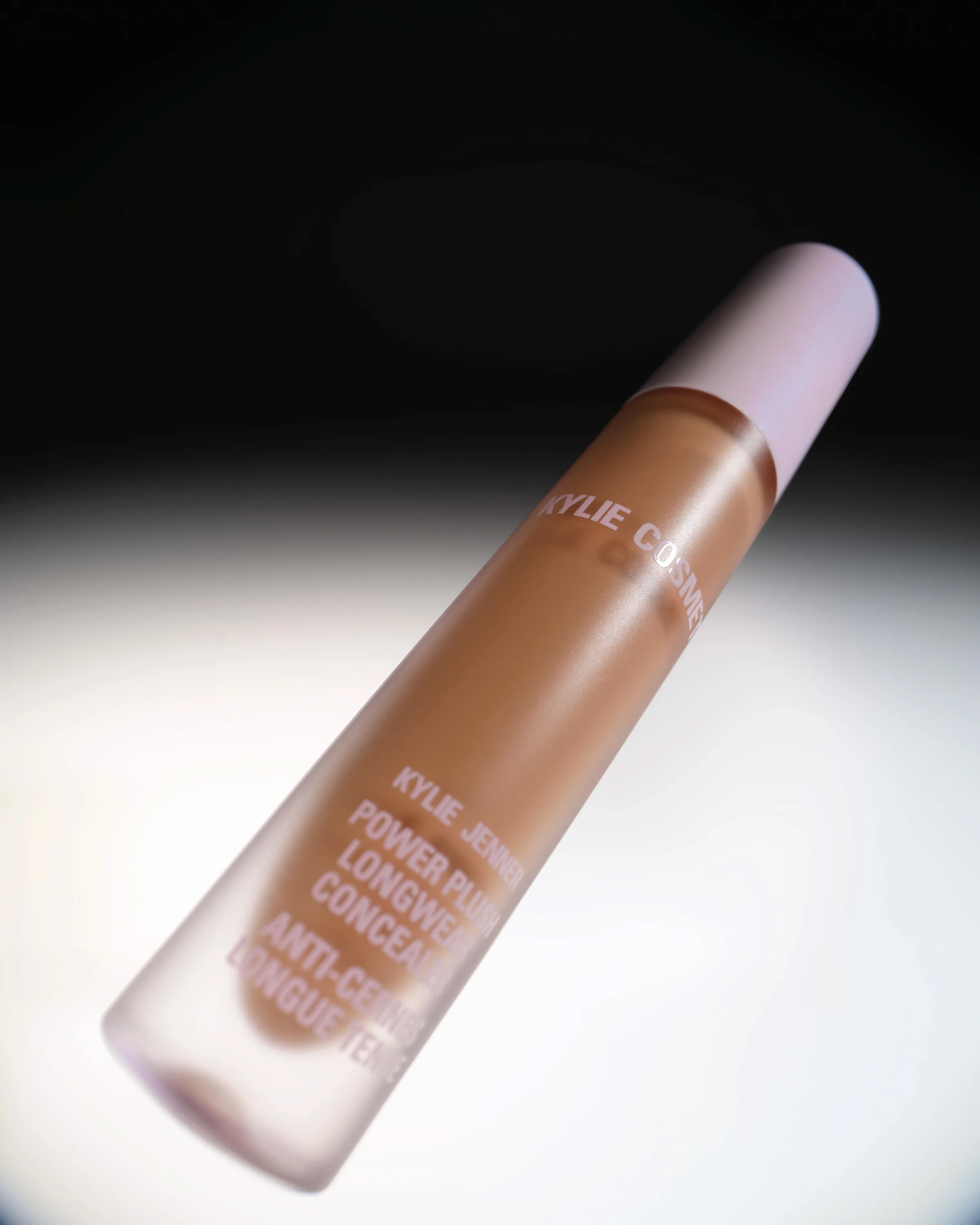 Frosted tube of Power Plush Longwear Concealer angled under a spotlight against a black background, for Kylie Cosmetics.
