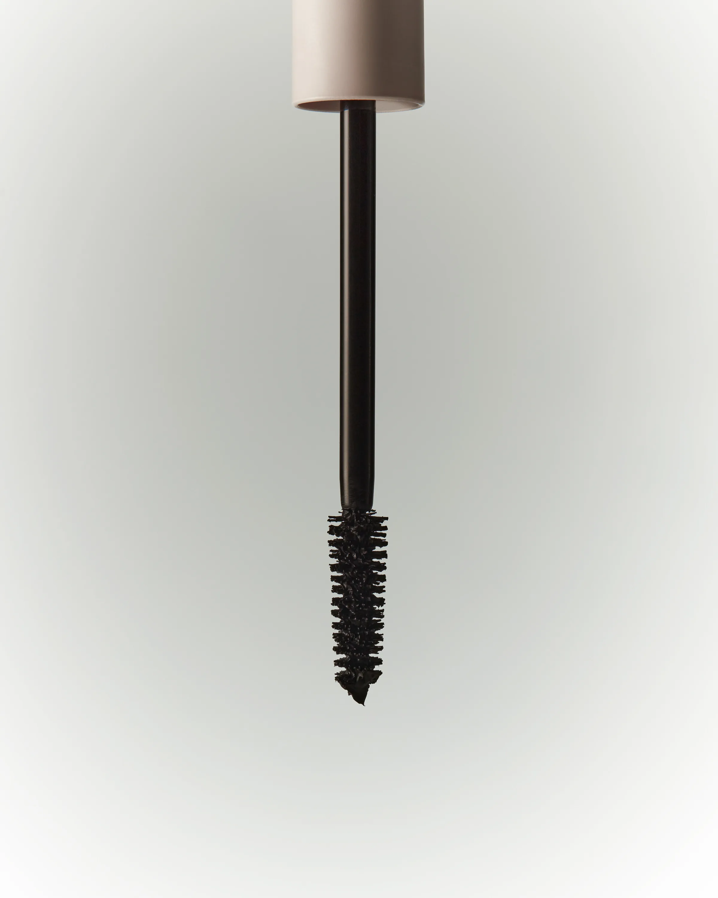 Mascara wand with black bristle brush and nude cap hanging against a soft grey backdrop, for Kylie Cosmetics.