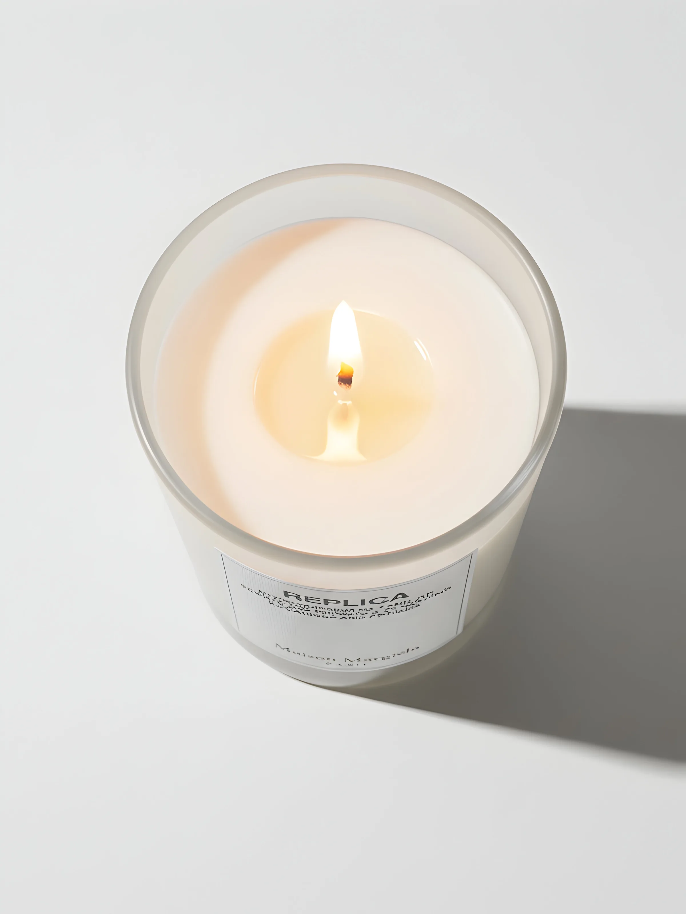 AI image of a lit Replica candle in a frosted glass jar, seen from above on white with a hard shadow. Maison Margiela AI Concept.
