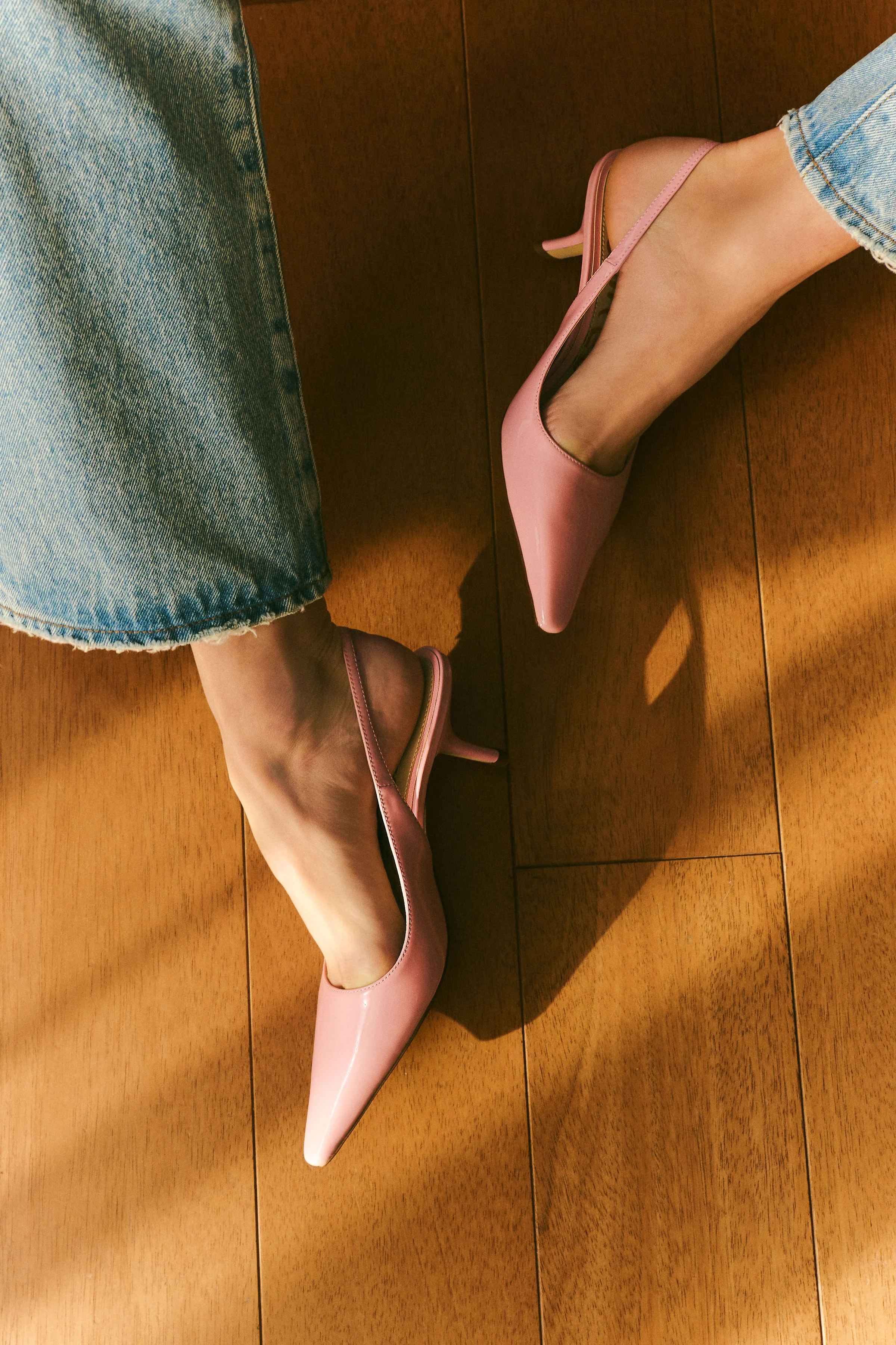 Pink patent slingback kitten heels worn with faded jeans on a sunlit wooden floor, for Sam Edelman.
