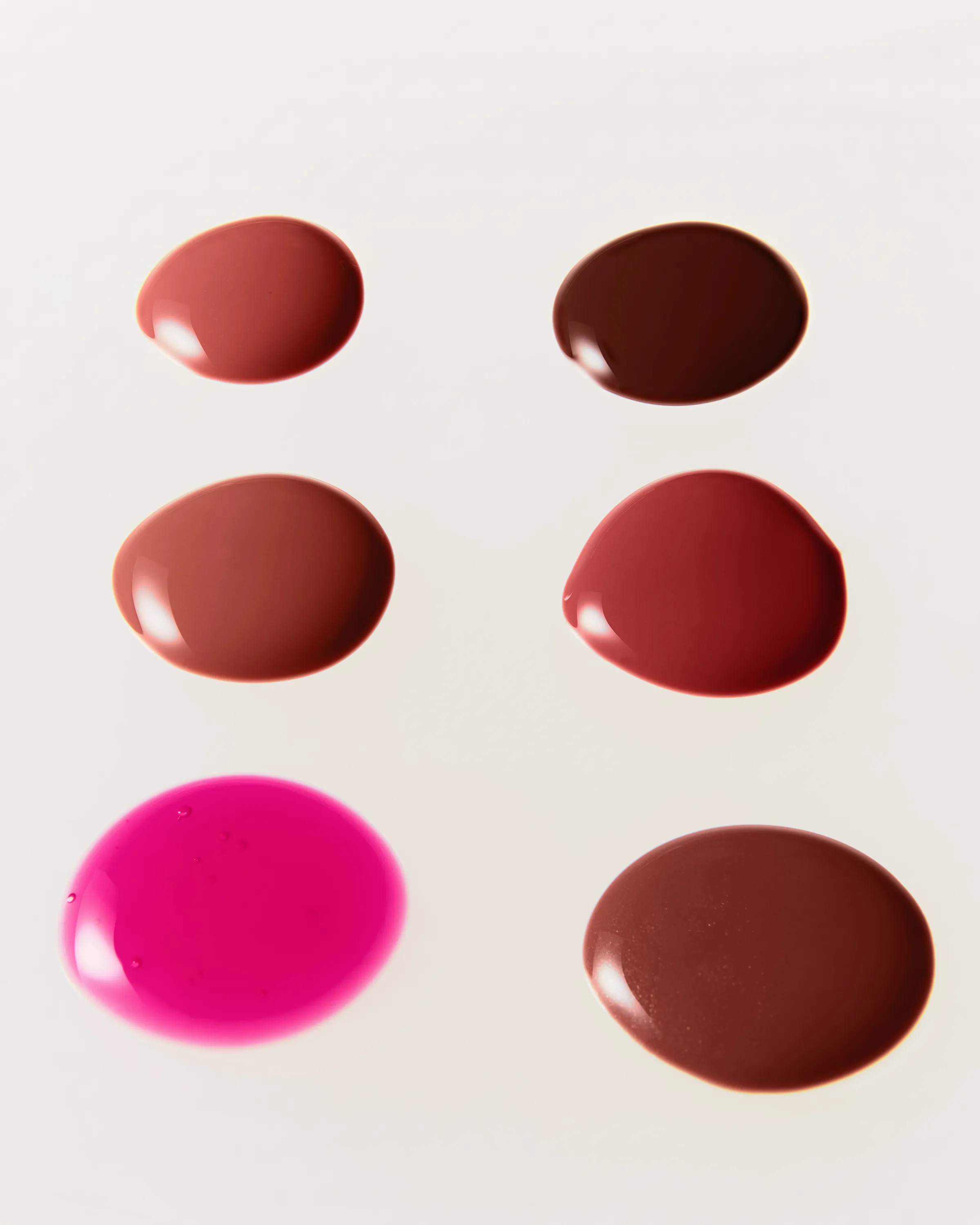 Six glossy lip glaze swatches in nude, brown, berry and hot pink shades on a white surface, for Kylie Cosmetics.