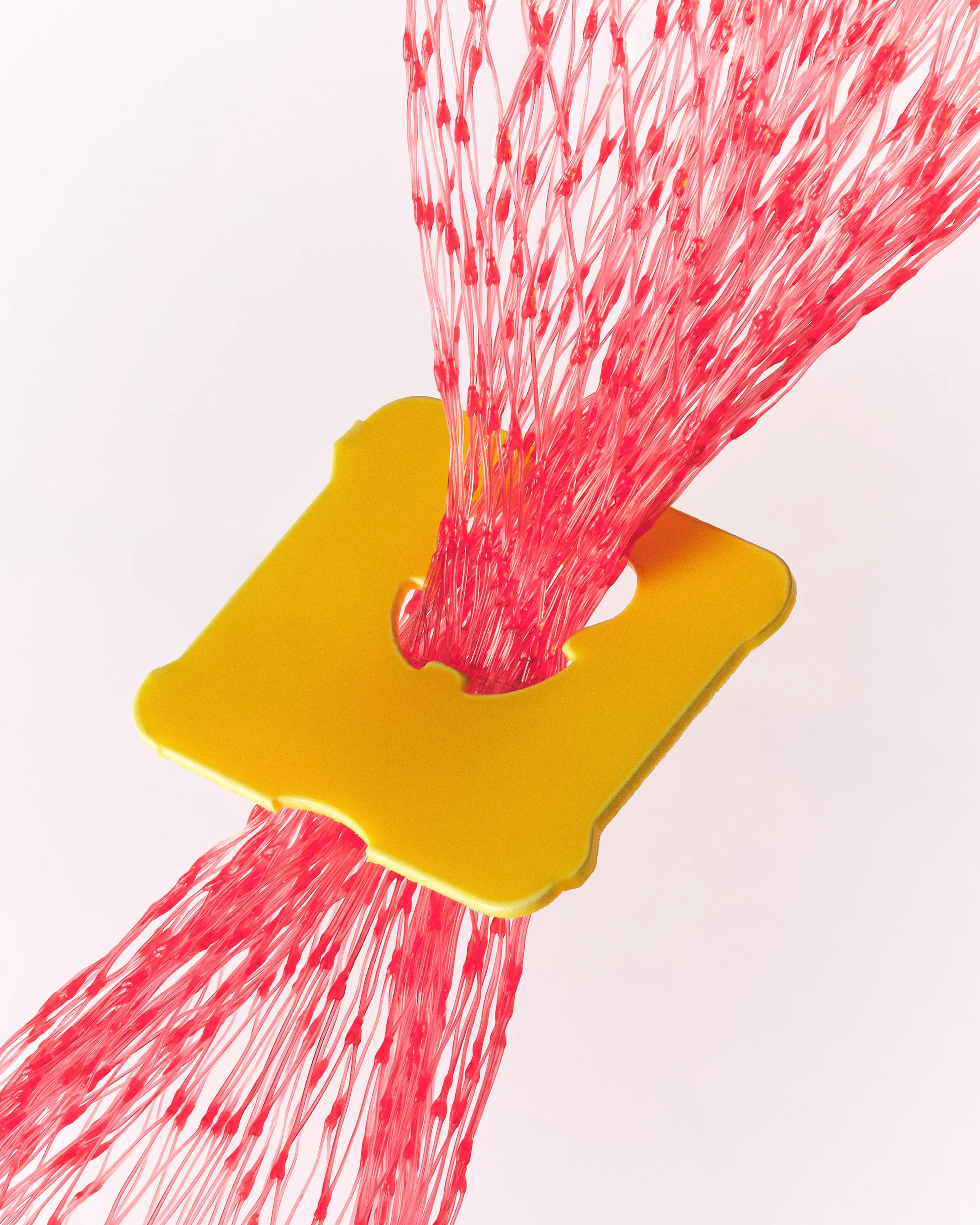 Still life of a yellow plastic bag clip cinching red mesh netting against a white background, for Kylie Cosmetics.