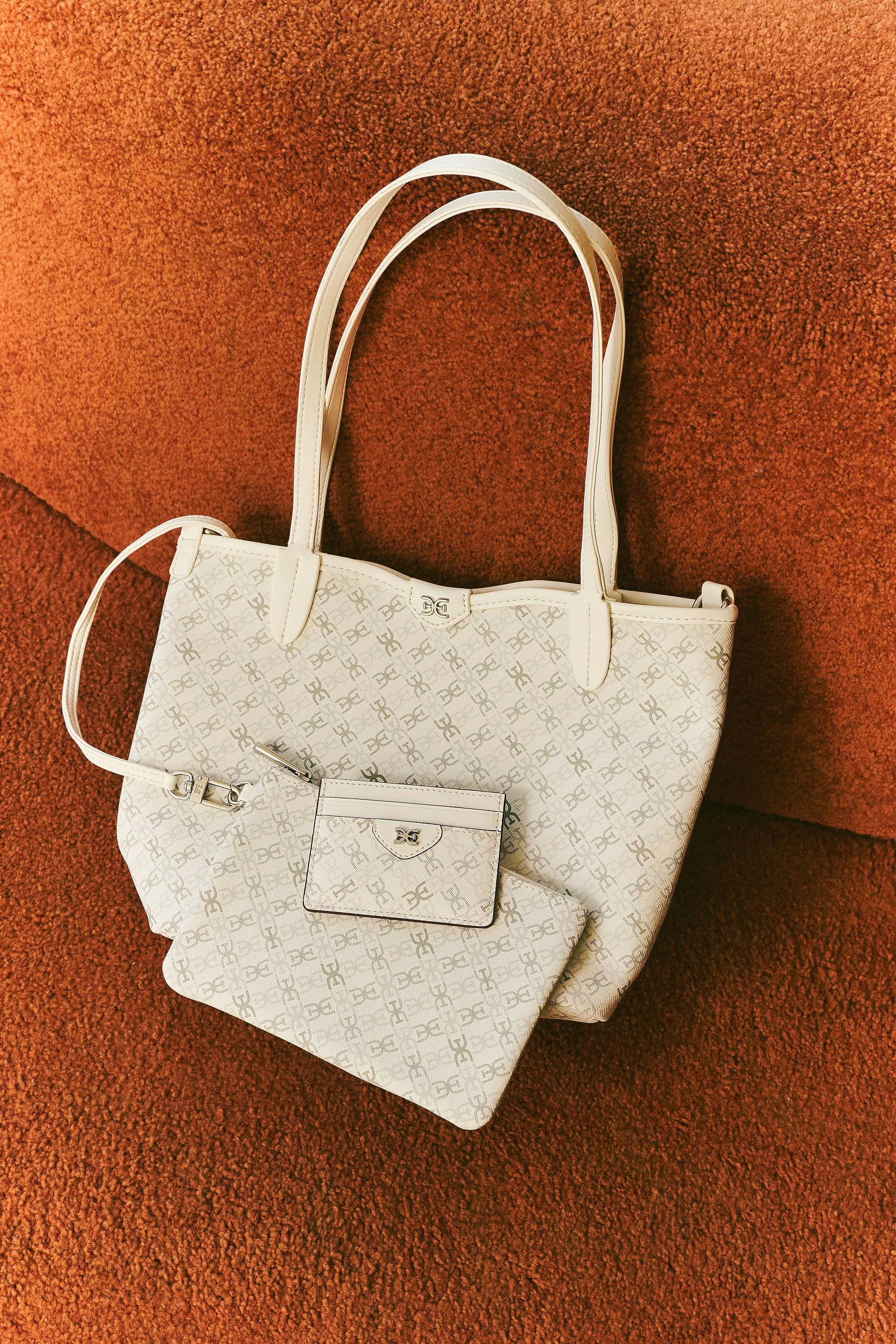 Cream monogram tote with matching pouch and card holder on a rust-orange textured sofa, for Sam Edelman.