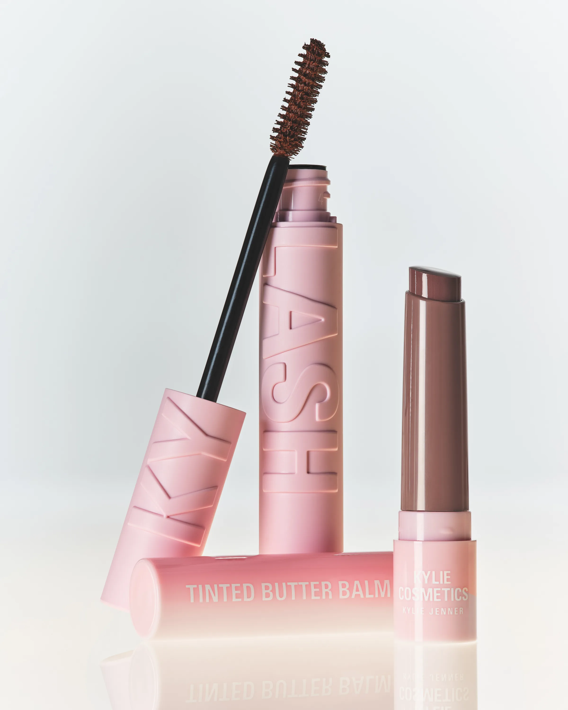 Still life of pink Kylash mascara with brown wand and Mocha Kiss Tinted Butter Balm on white, for Kylie Cosmetics.