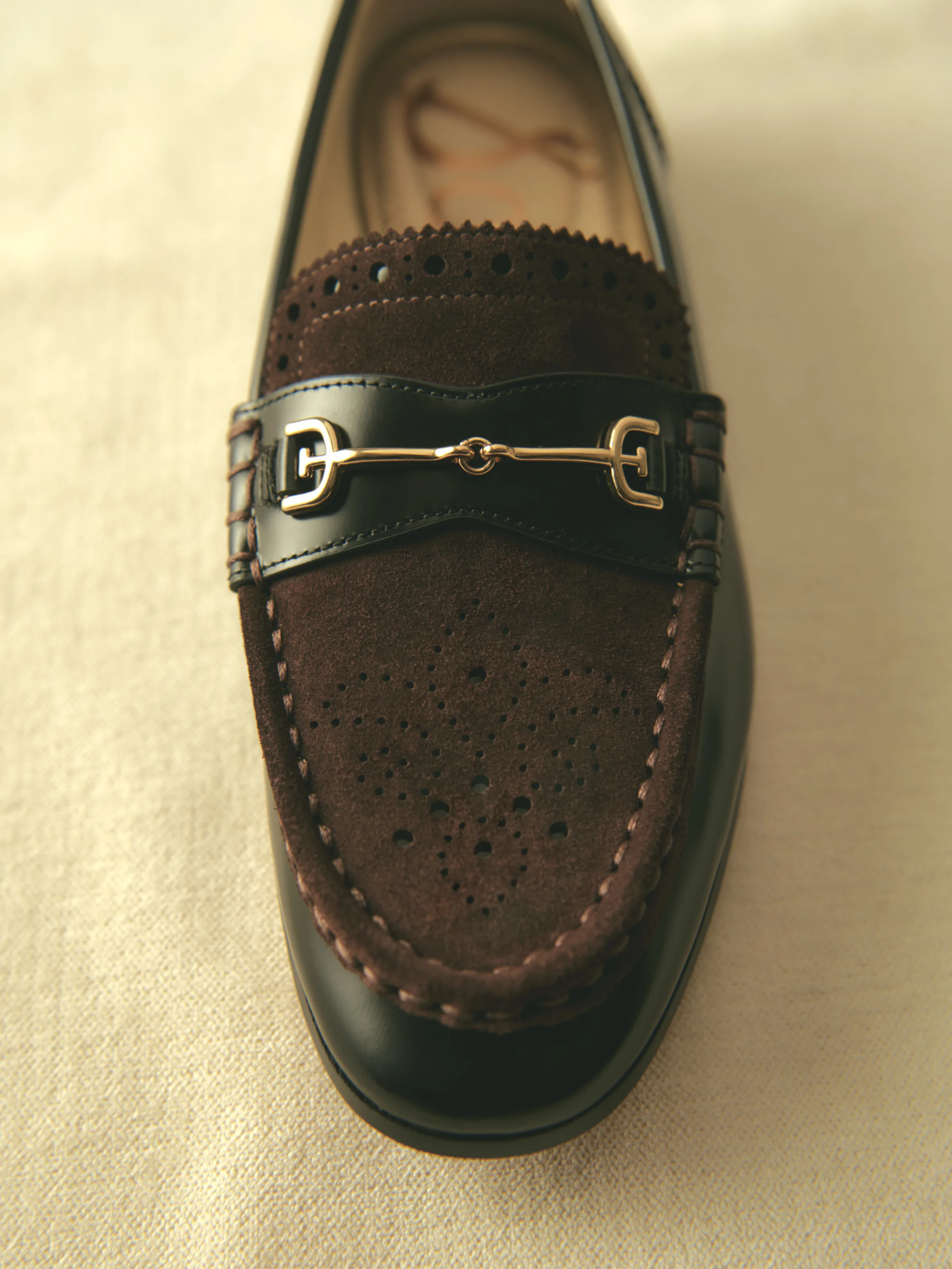 Black leather loafer with brown perforated suede vamp and gold horsebit hardware on cream fabric, for Sam Edelman.