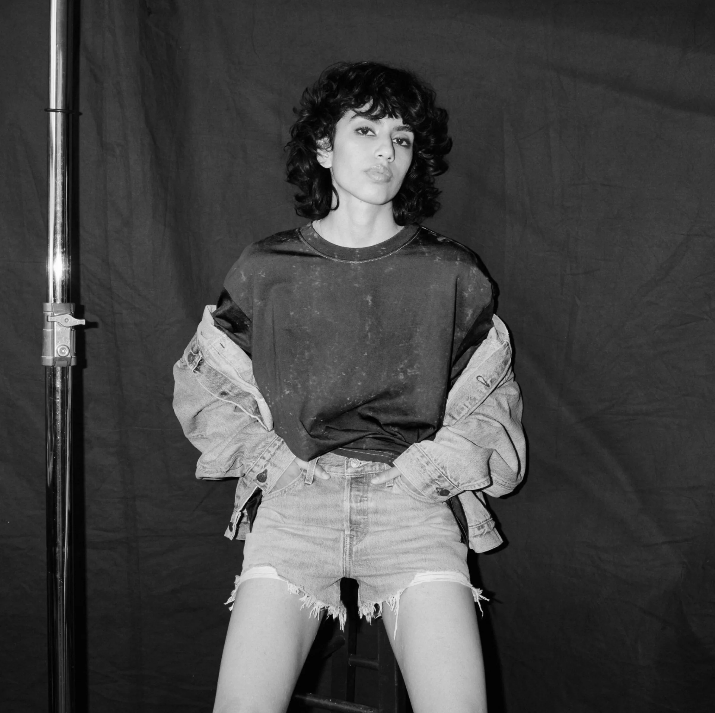 Black and white portrait of a curly-haired model in a denim jacket and cutoff shorts against dark backdrop, for Levi's.