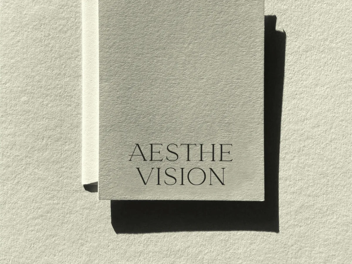 Pale grey textured card printed with the Aesthe Vision wordmark, casting a hard shadow on paper, for Aesthevision.