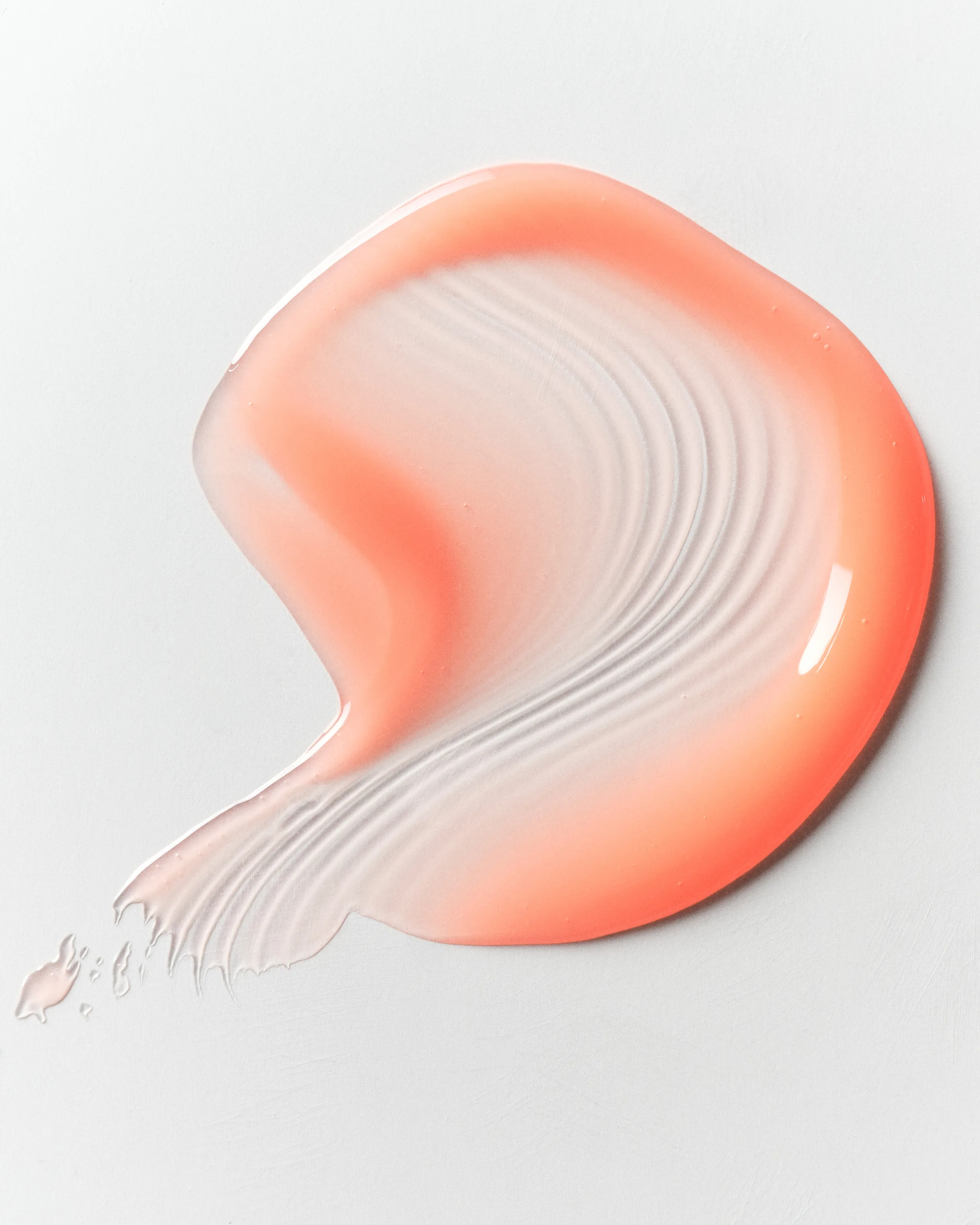 Swirled swatch of glossy coral lip product with ridged texture on a white surface, for Kylie Cosmetics.
