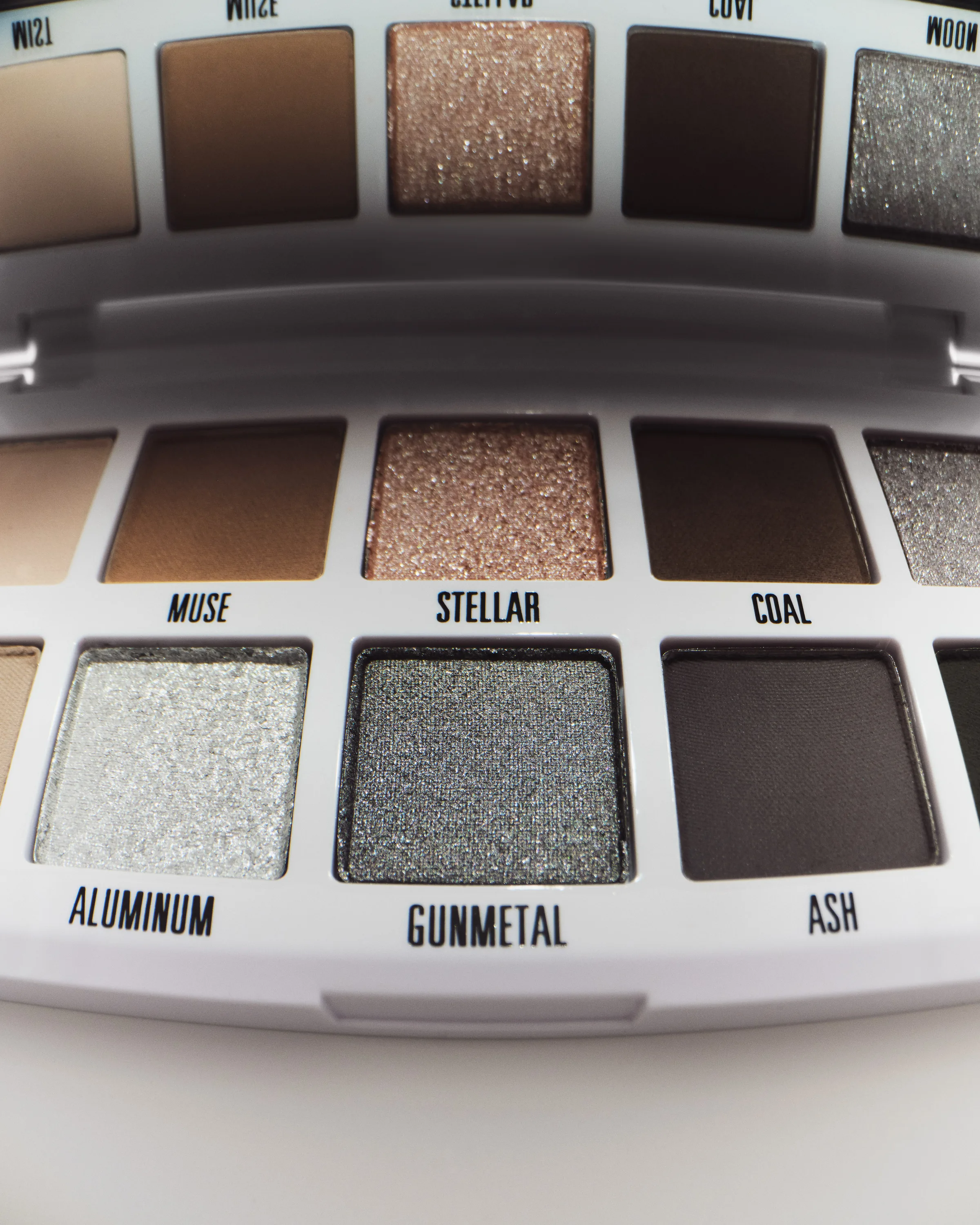Close-up of a white eyeshadow palette with smoky shades like Muse, Stellar, Coal, Gunmetal and Ash, for Kylie Cosmetics.