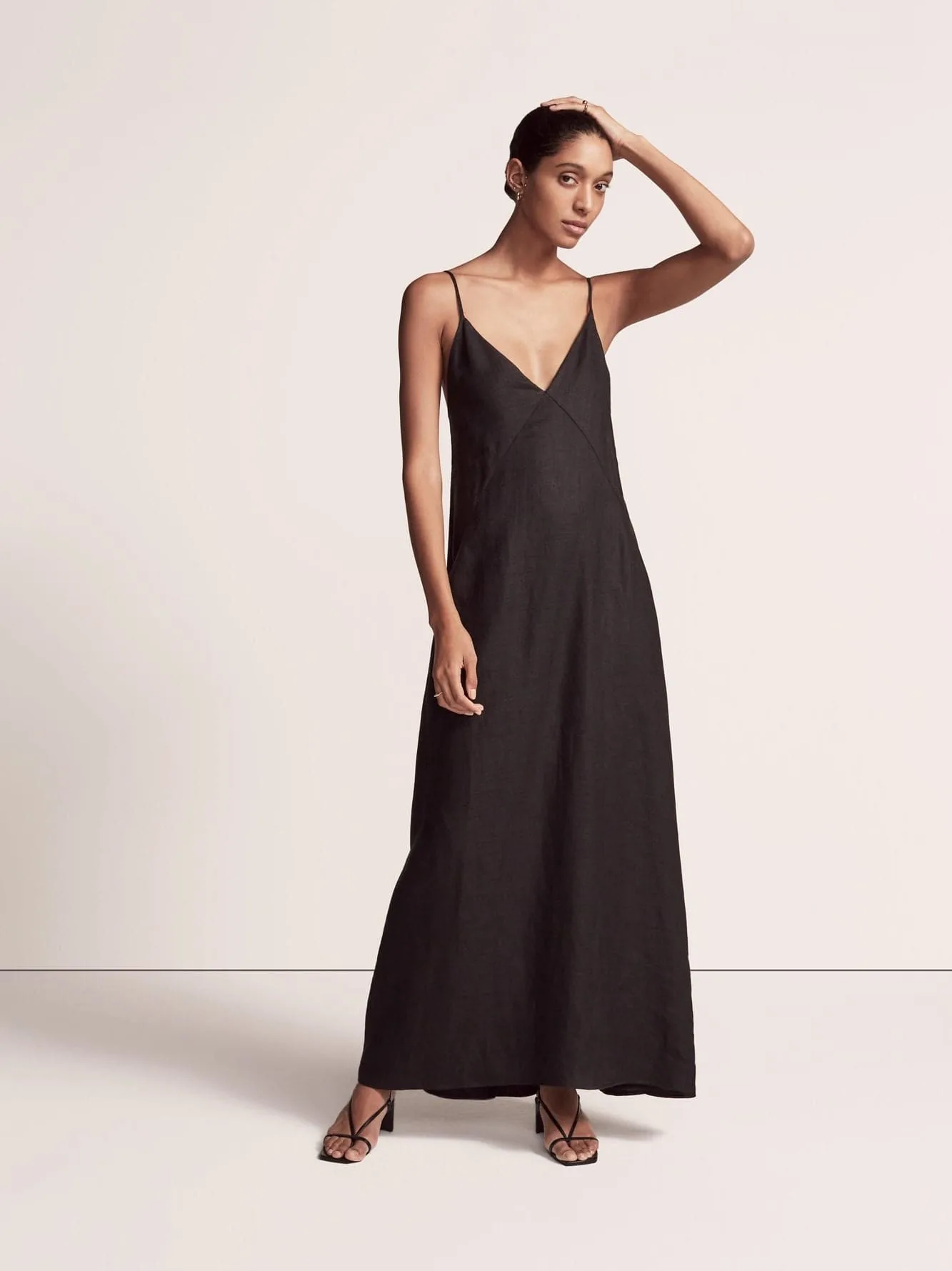 Model in a black linen slip maxi dress and strappy sandals on a pale studio backdrop, for Another Tomorrow.