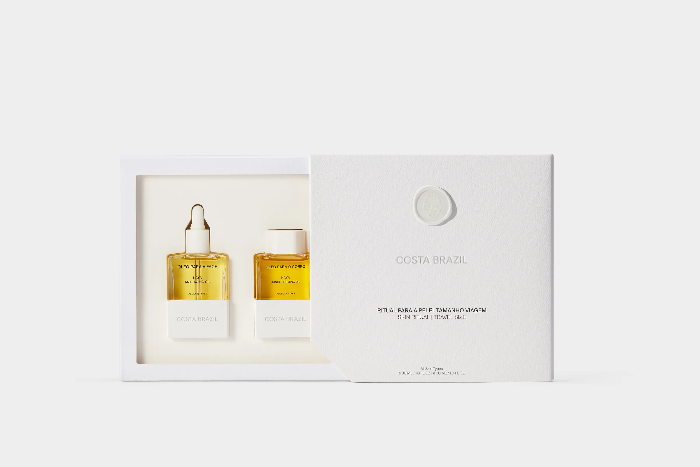 Two golden face and body oil bottles in an open white gift box with sleeve on a light grey backdrop, for Costa Brazil.