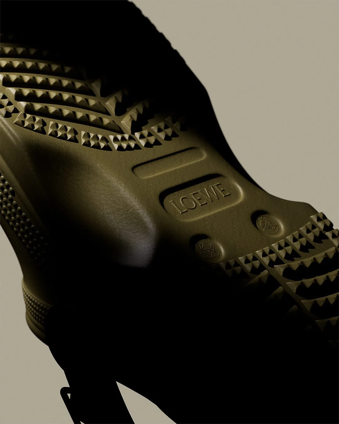 CGI render of an olive rubber boot sole with embossed logo and studded tread in dramatic shadow, for Loewe.