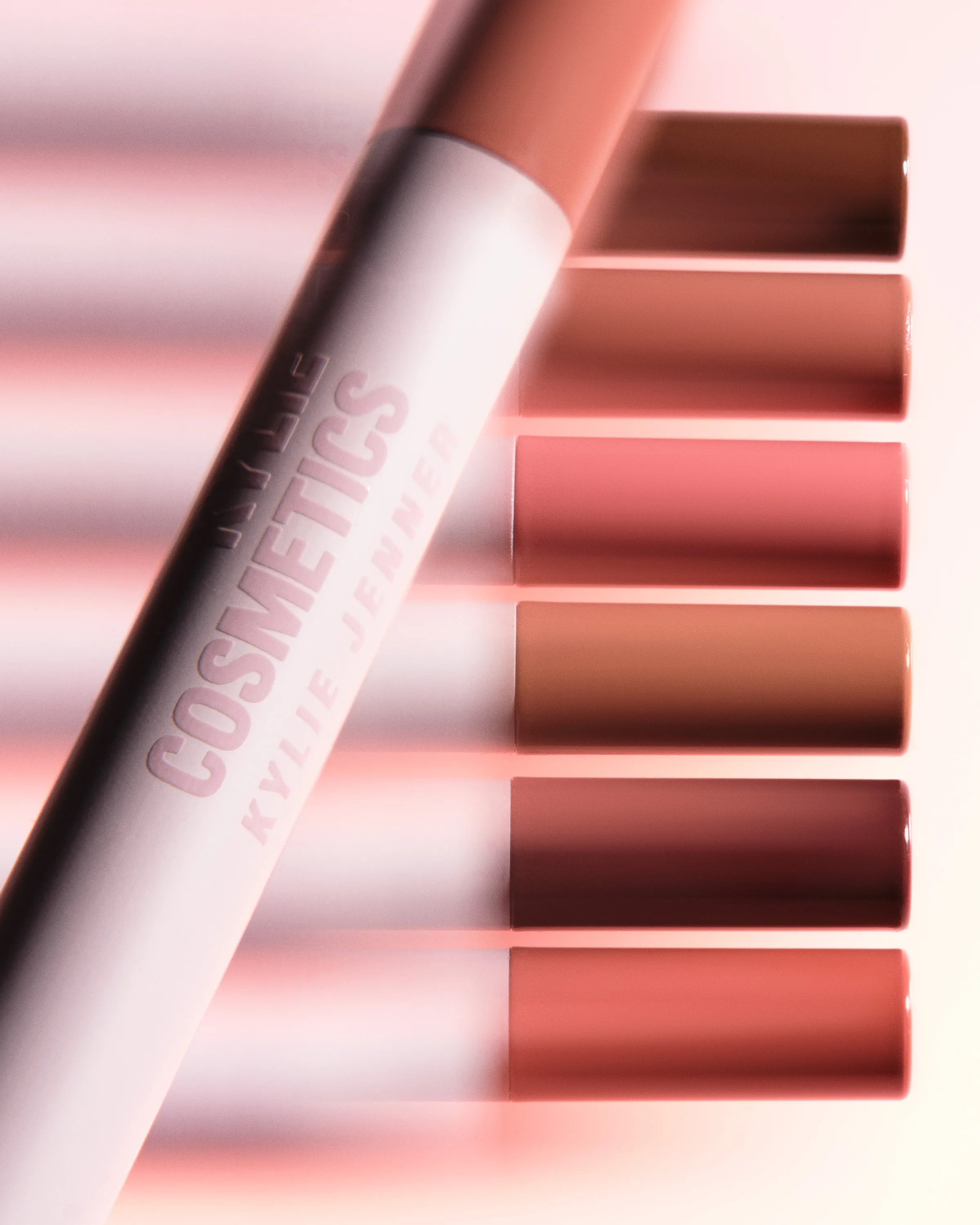 White lip liner pencil laid diagonally across six nude and rose liner tips on a soft pink backdrop, for Kylie Cosmetics.